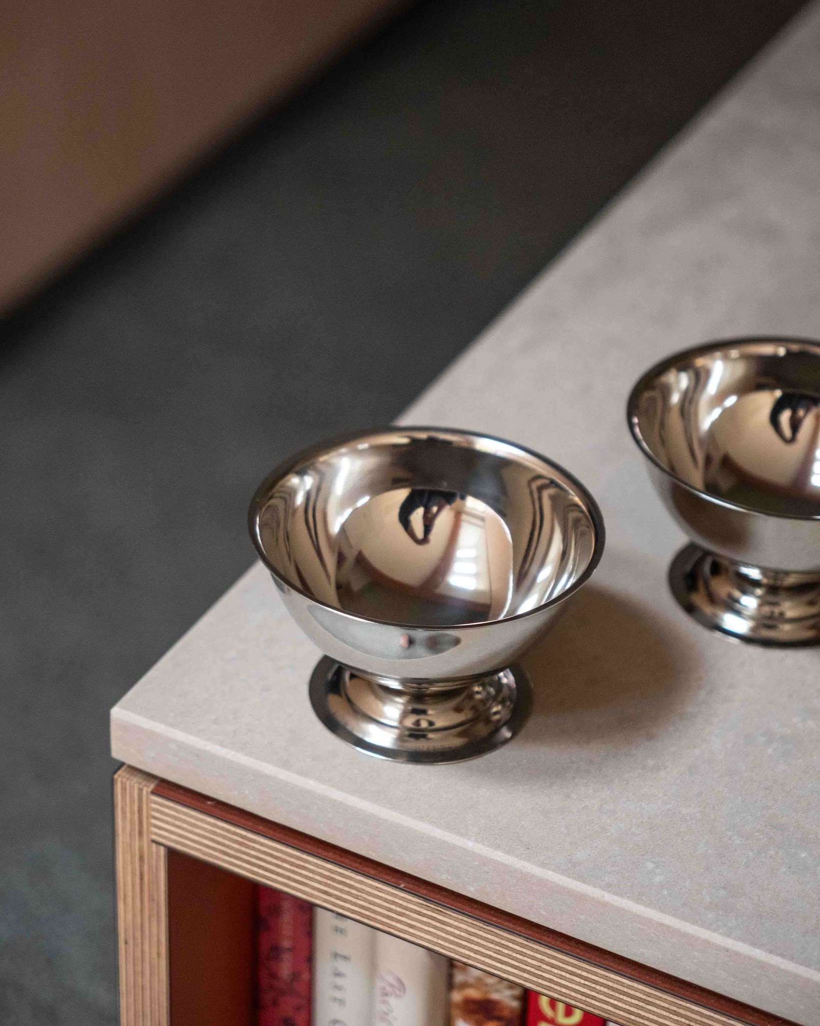Pair of stainless steel ice cream coupes on a stone worktop above plywood shelving.