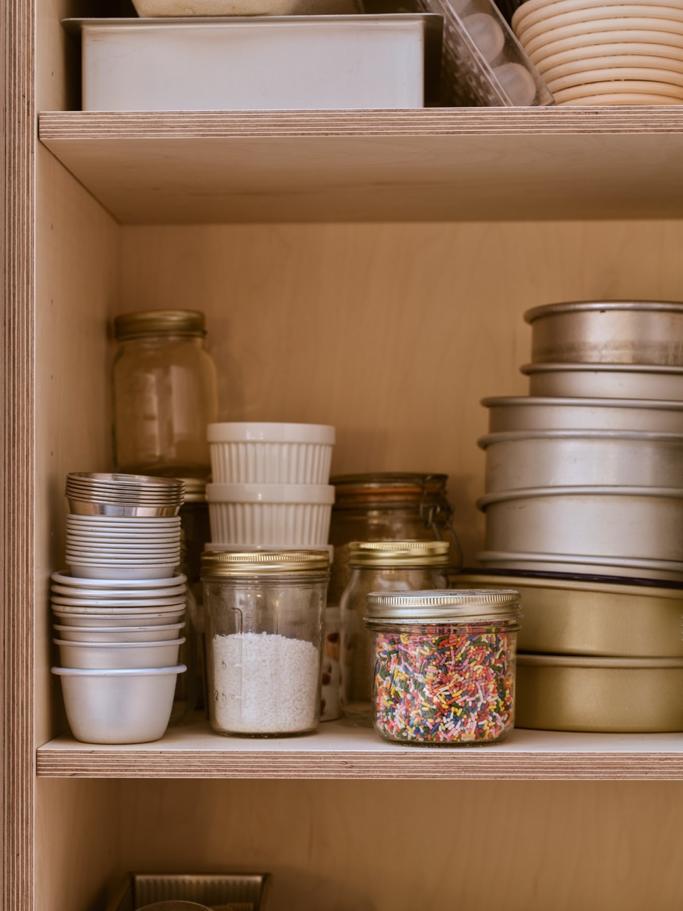 Custom baking storage in baker Edd Kimber’s Walthamstow kitchen, designed by Uncommon Projects with maple veneer plywood shelving for cake tins, ramekins, jars and baking ingredients.