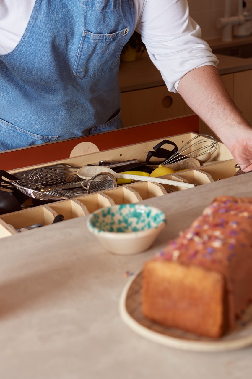 Baker Edd Kimber using a custom utensil drawer in his bespoke Uncommon Projects kitchen, designed with plywood dividers to organise baking tools and equipment.