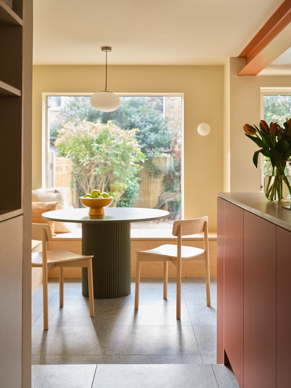 Dining area beside baker Edd Kimber’s bespoke Uncommon Projects kitchen in Walthamstow, with built-in seating and views to the garden beyond the kitchen extension.