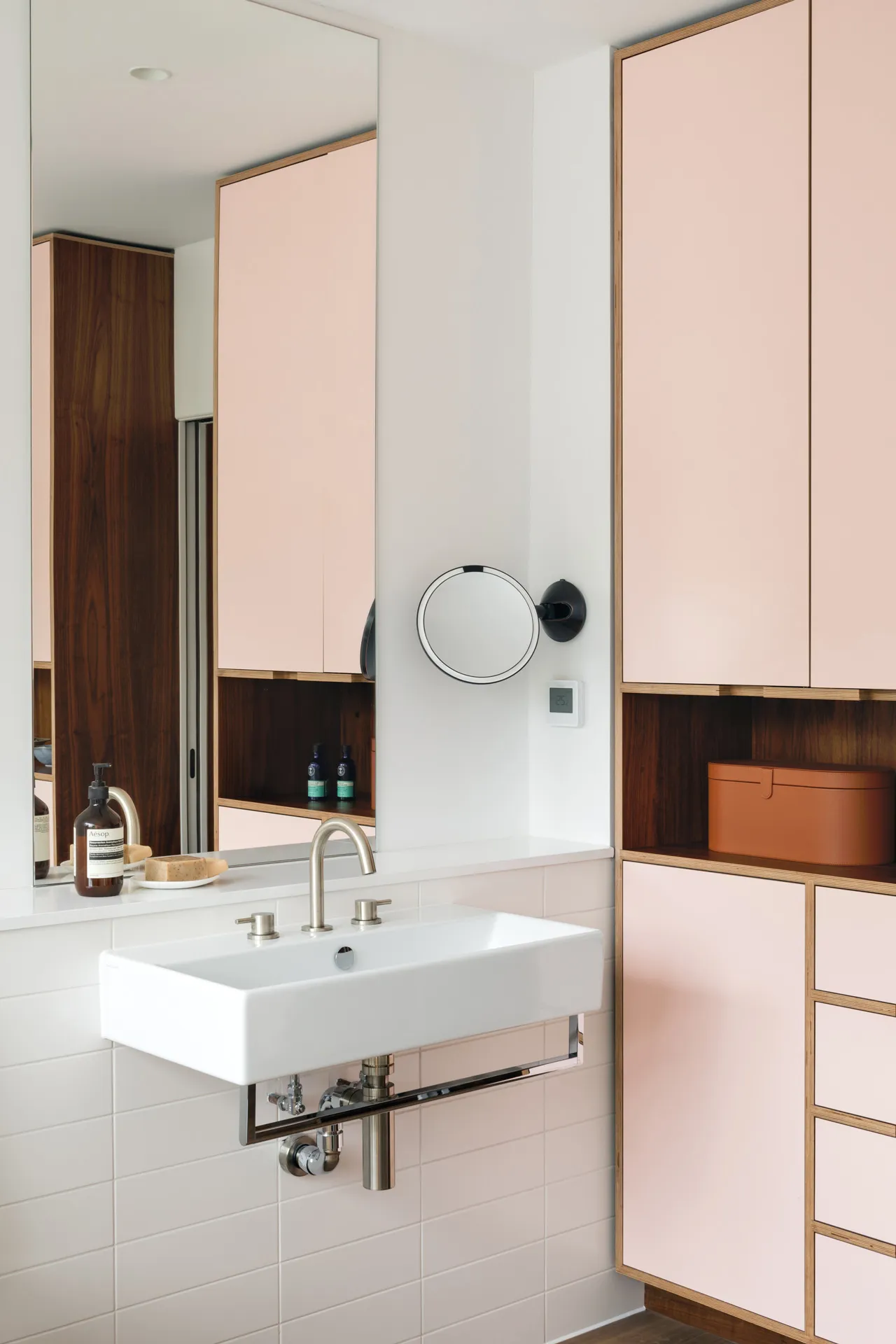 Pale pink doors contrast against these walnut-veneered bathroom cabinets.