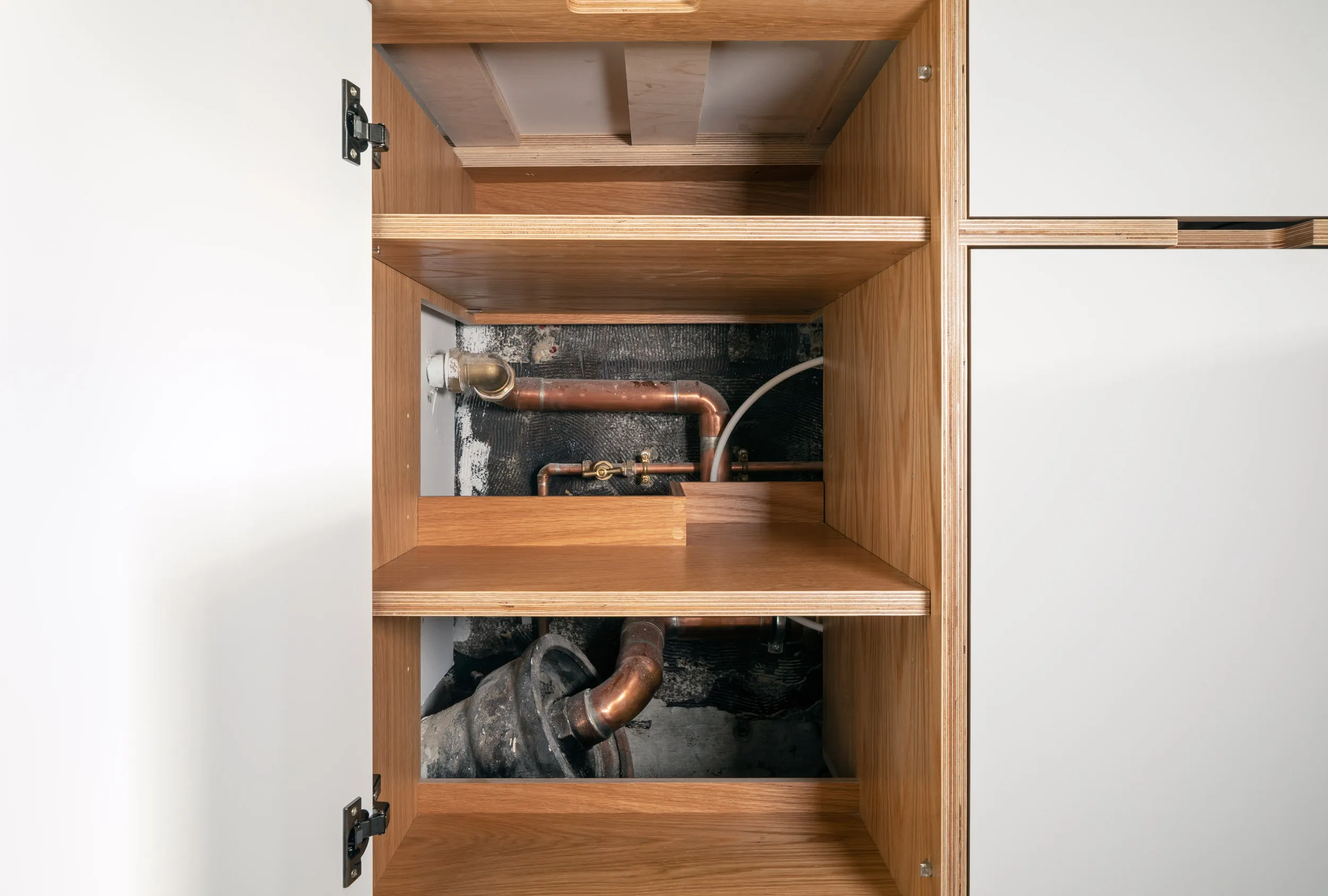 Concealed pipework in back of a bespoke plywood cabinet