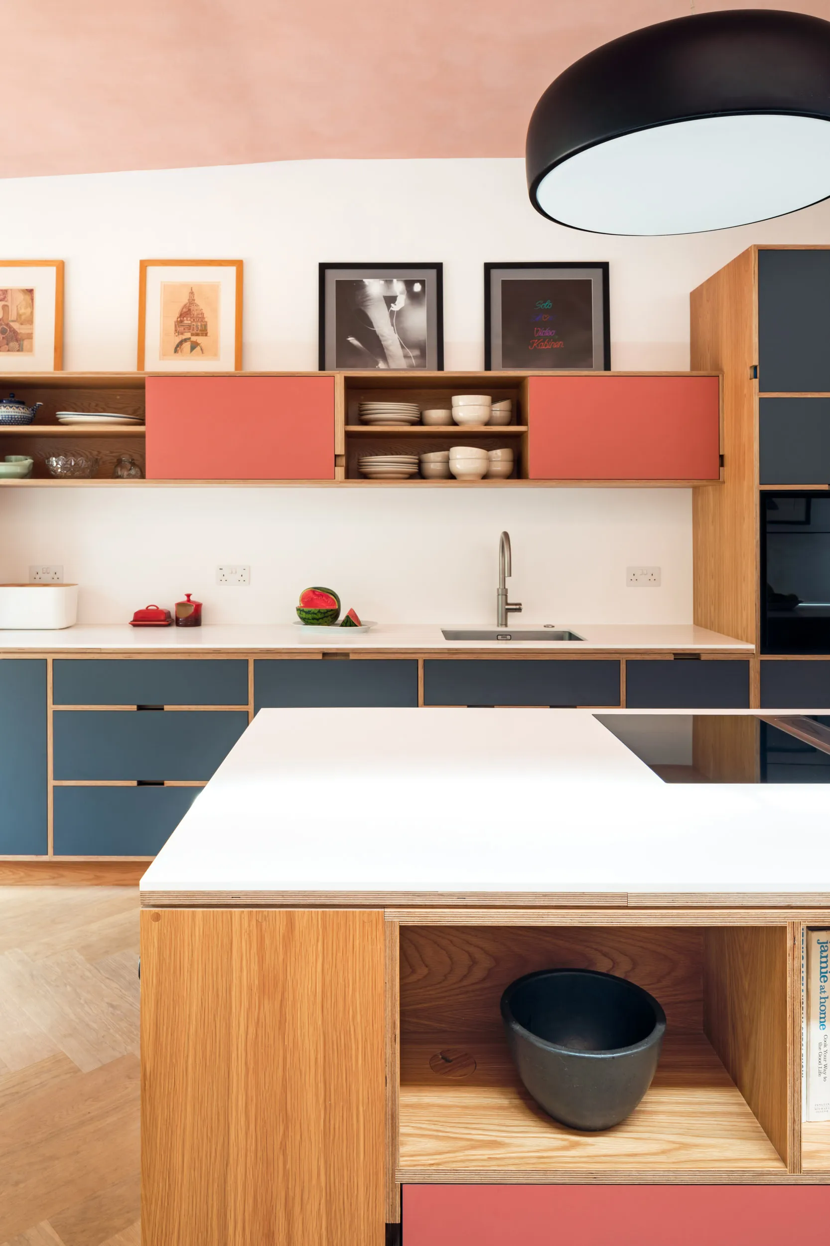 Close crop of oak plywood kitchen with pink and grey doors. and island