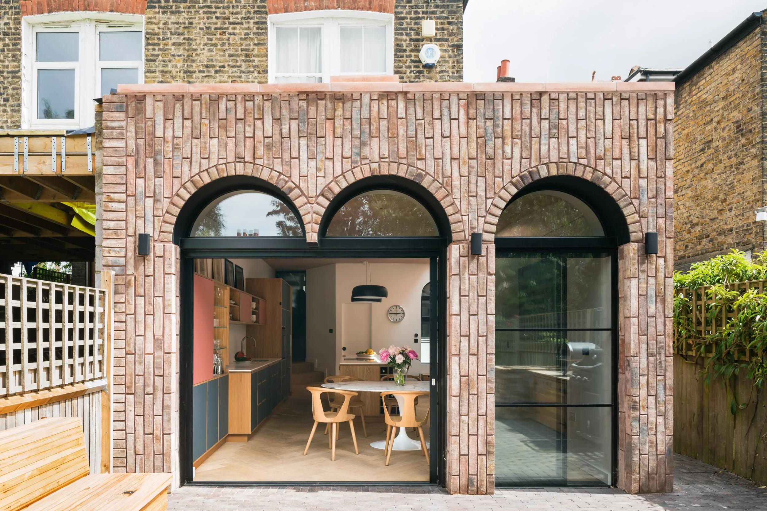 External view of extension with arched glazing and wide doors. Bespoke plywood kitchen inside.