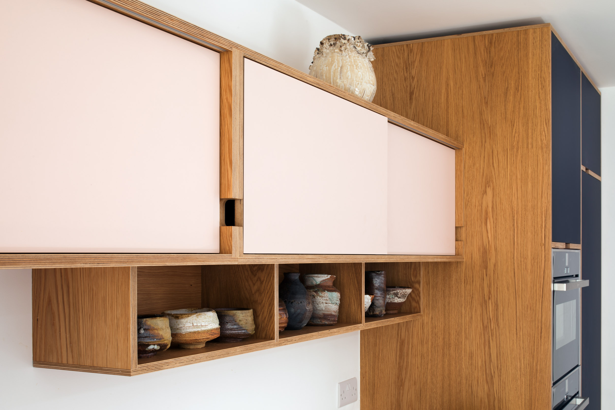Pink and oak veneered birch plywood wall cabinet with ceramics displayed