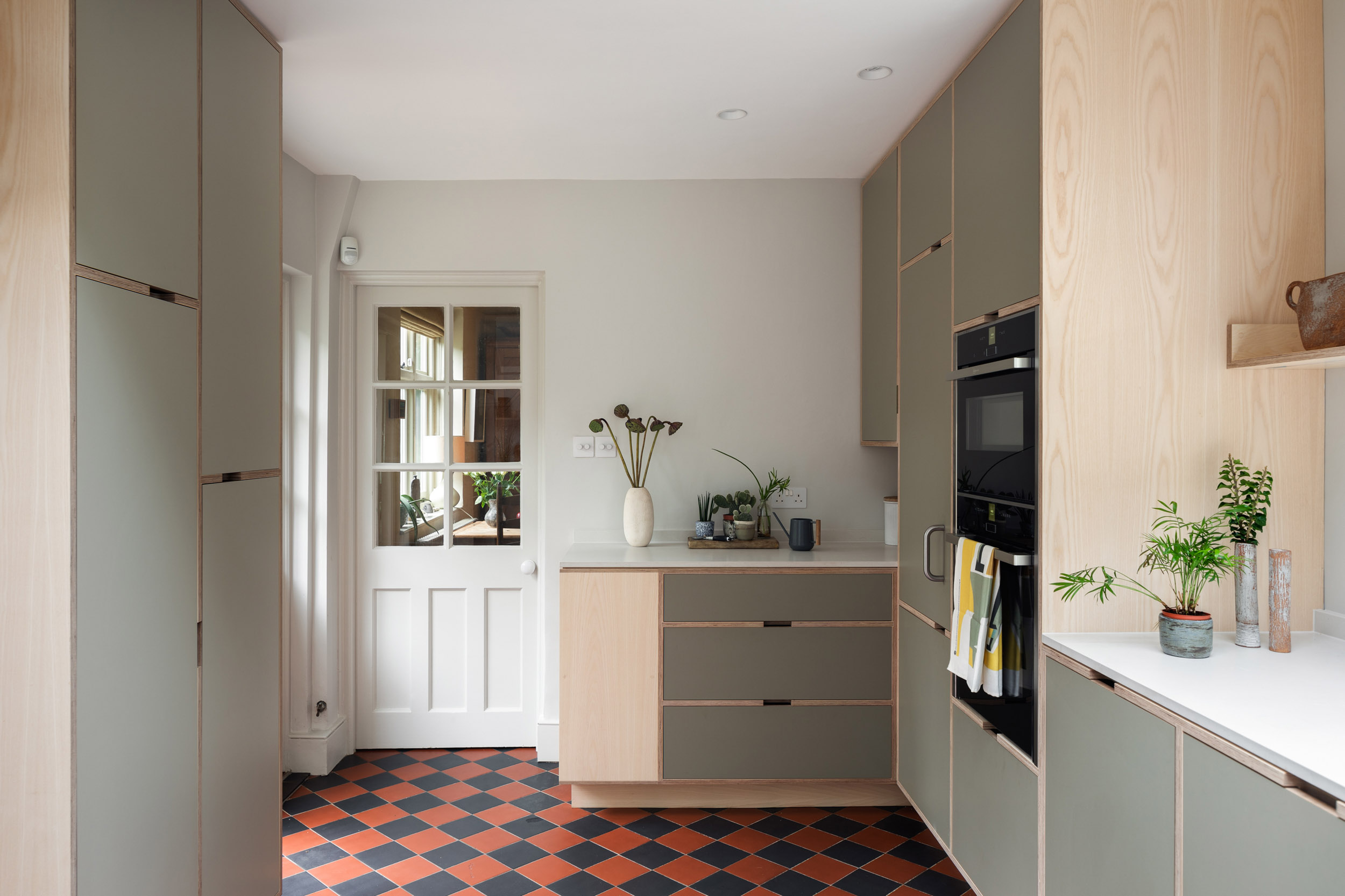 Contemporary plywood kitchen with ash veneer wall units, integrated ovens and terracotta flooring in a renovated Victorian home by Uncommon Projects.