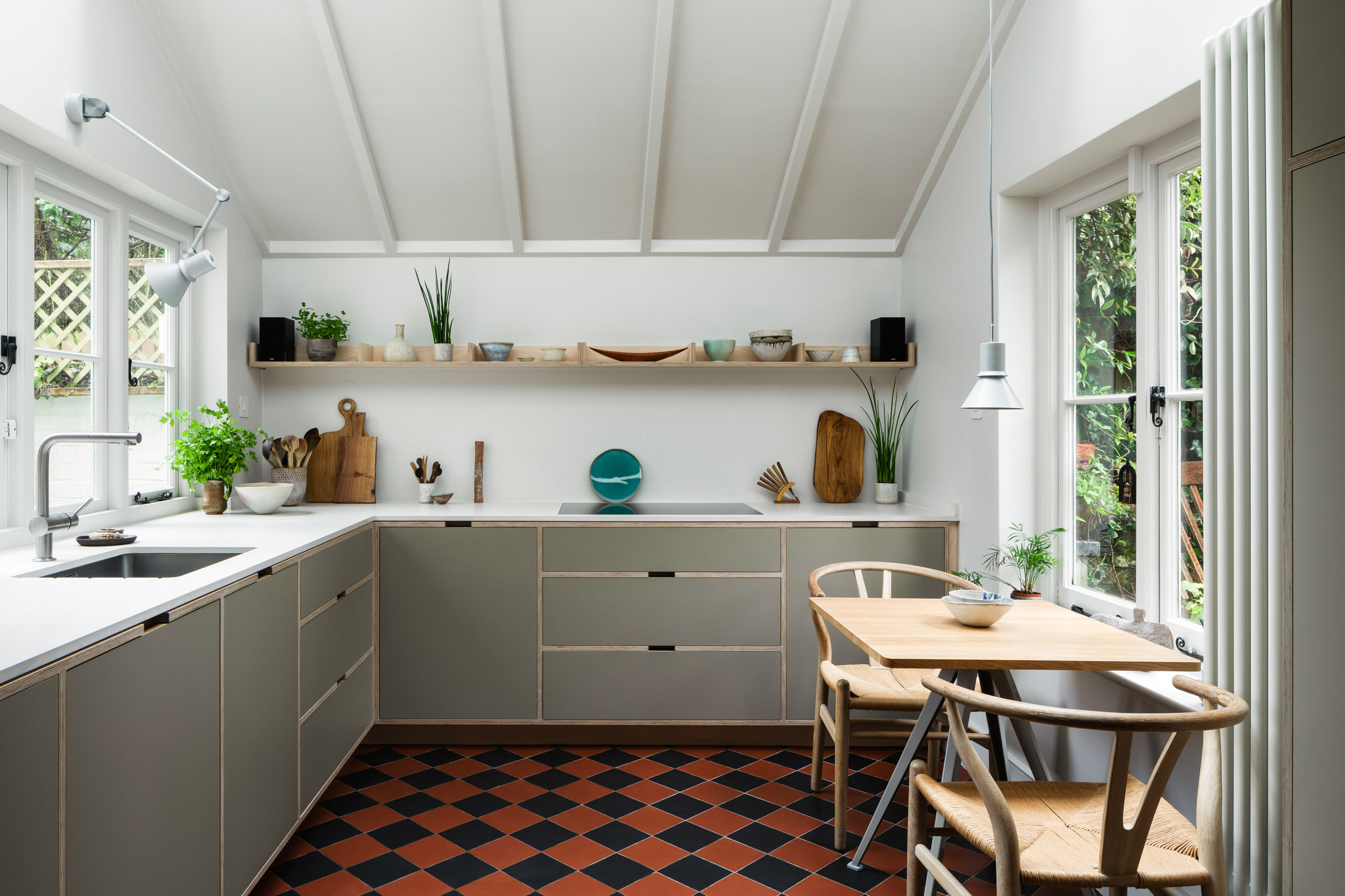 Green grey plywood kitchen with tiled floor and open shelving, in a Hampstead cottage.