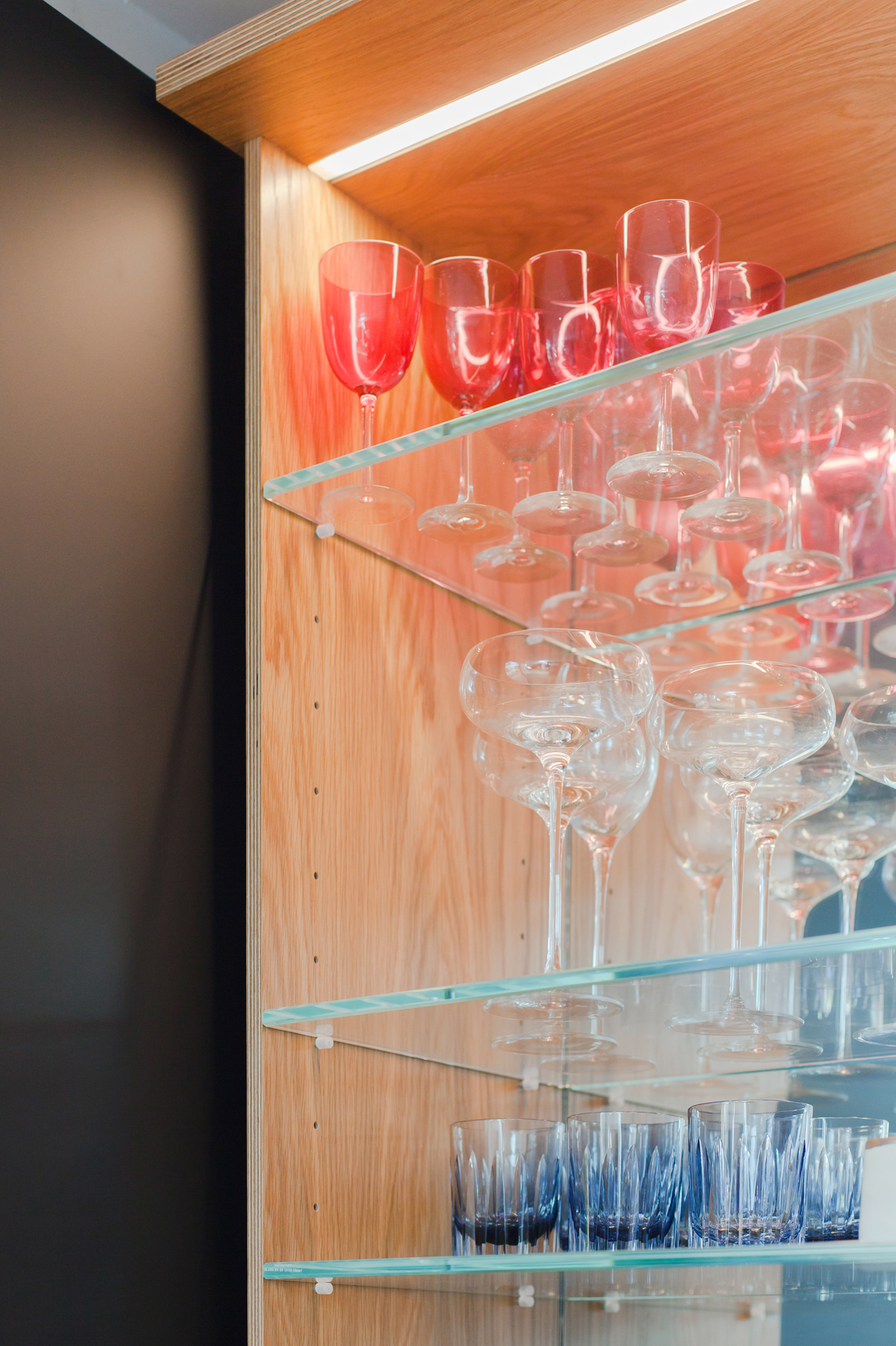 Plywood mirrored drinks cabinet detail with glassware and glass shelving.