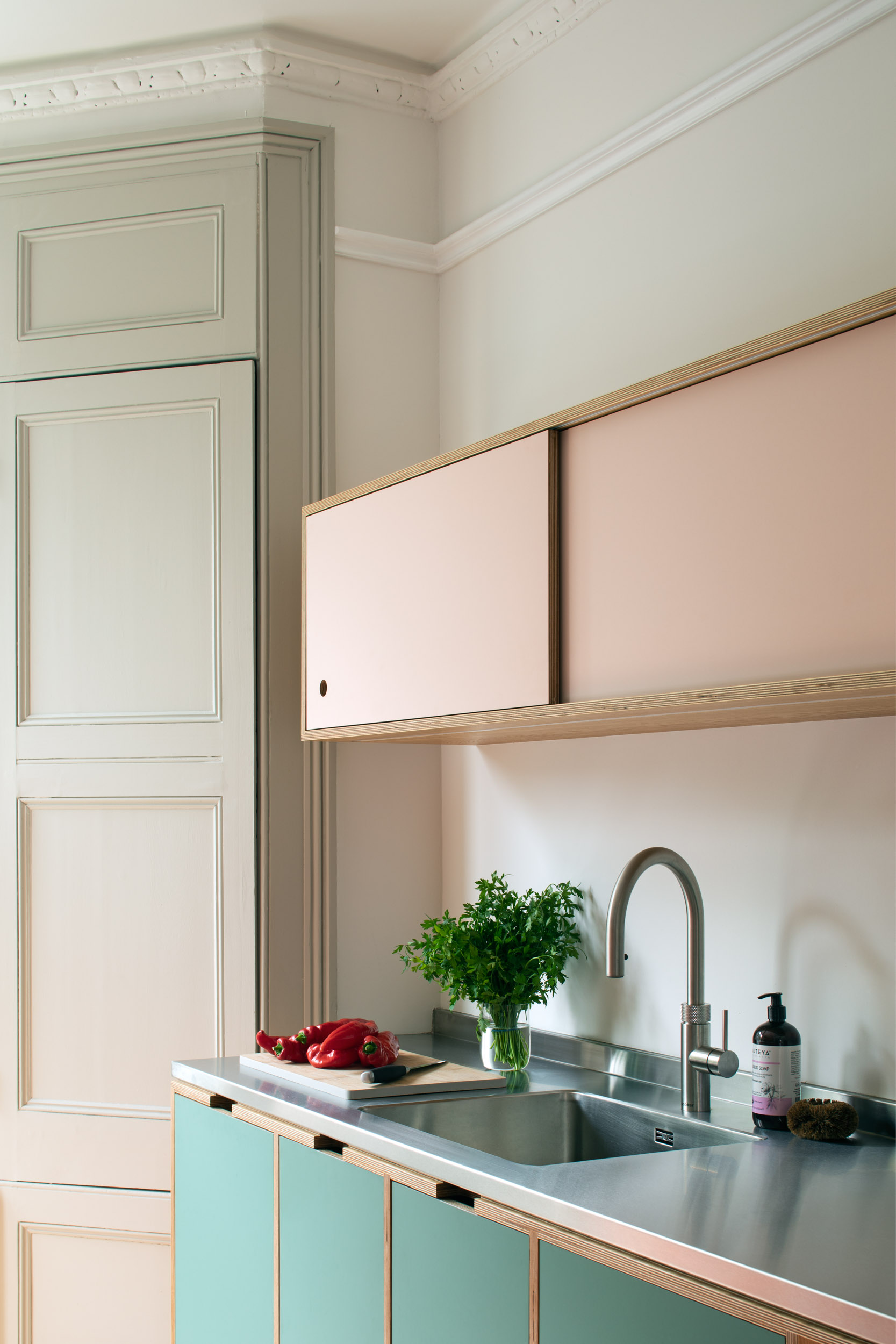 Close up detail of pink wall cubpoard, light green base units and stainless stell worktop