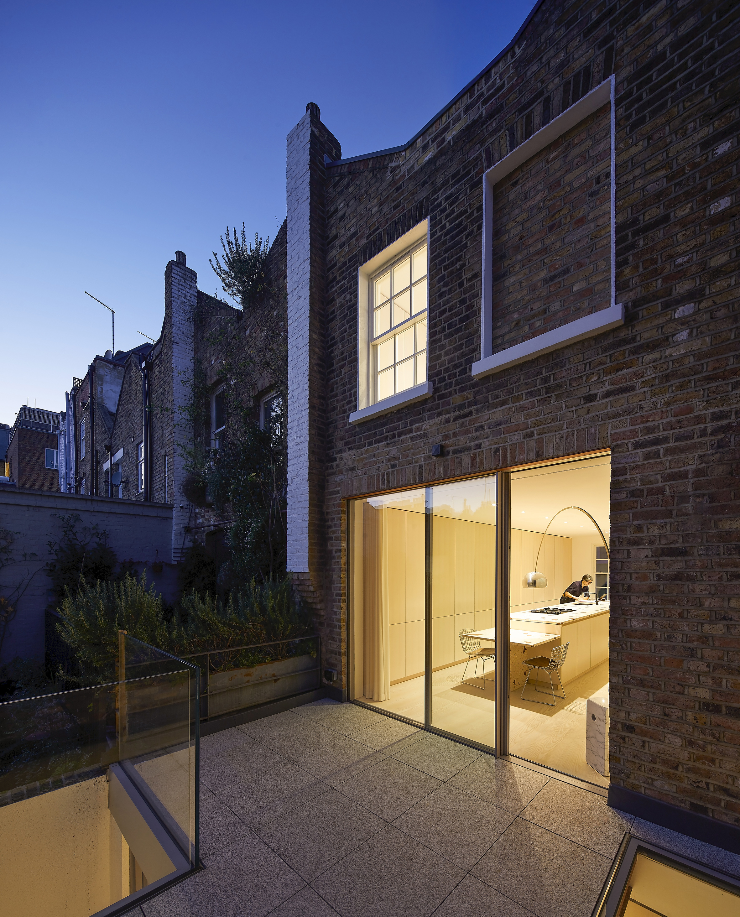 Outside night time looking into a brightly lit plywood kitchen 