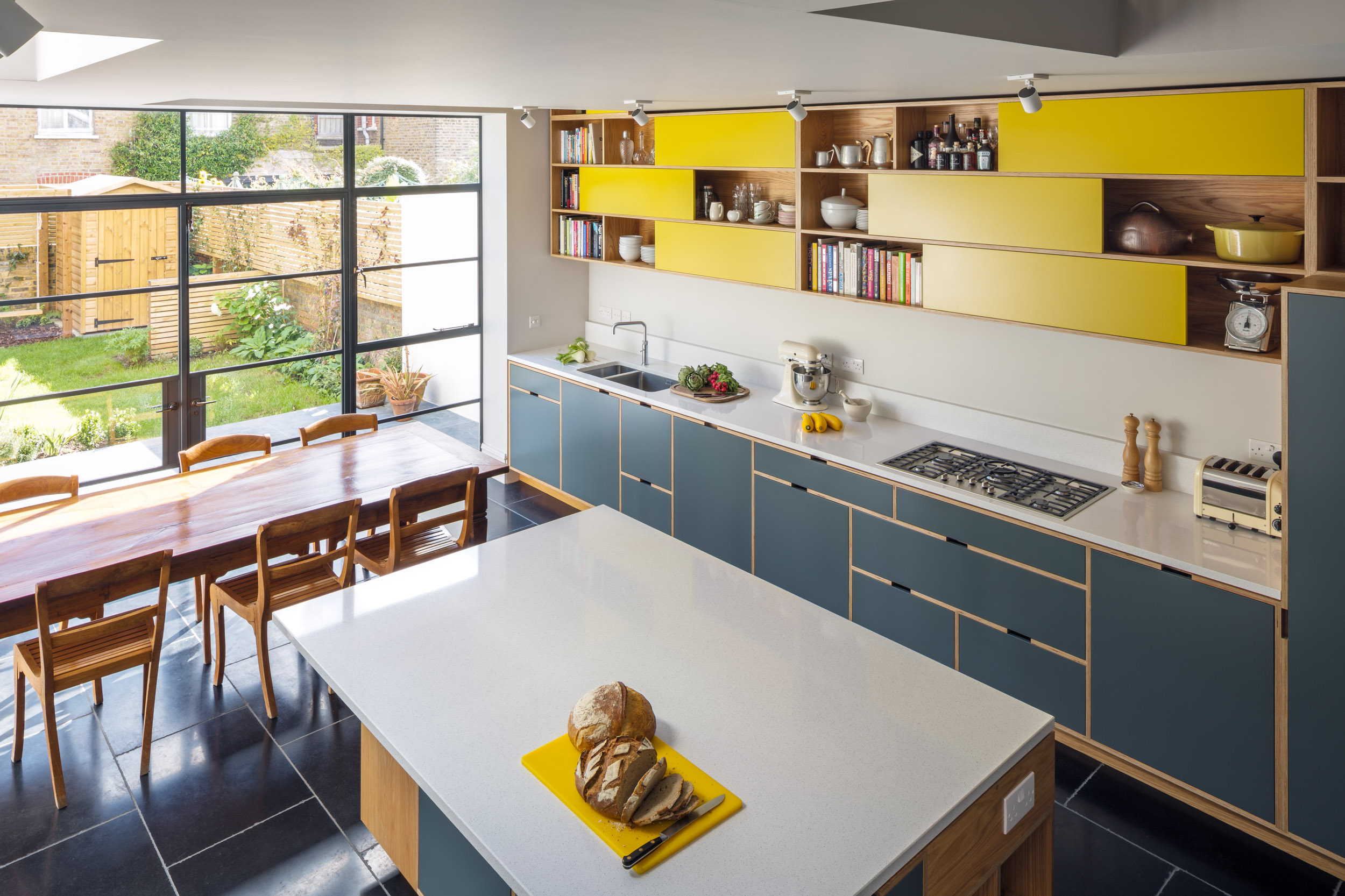 Looking down on a light grey plywood kitchen with yellow sliding door wall cabinets, with kitchen island.