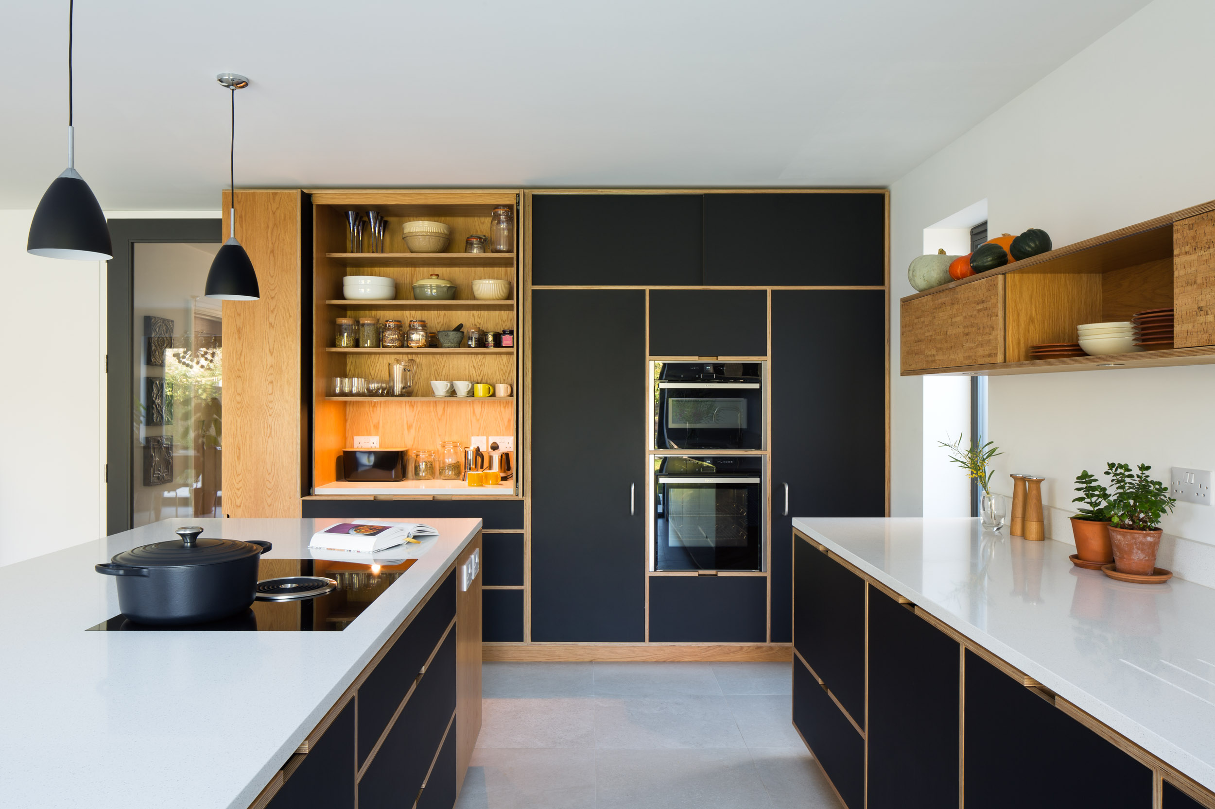 Large bank of black full height kitchen cabinetry including pantry cupboard with pocket doors