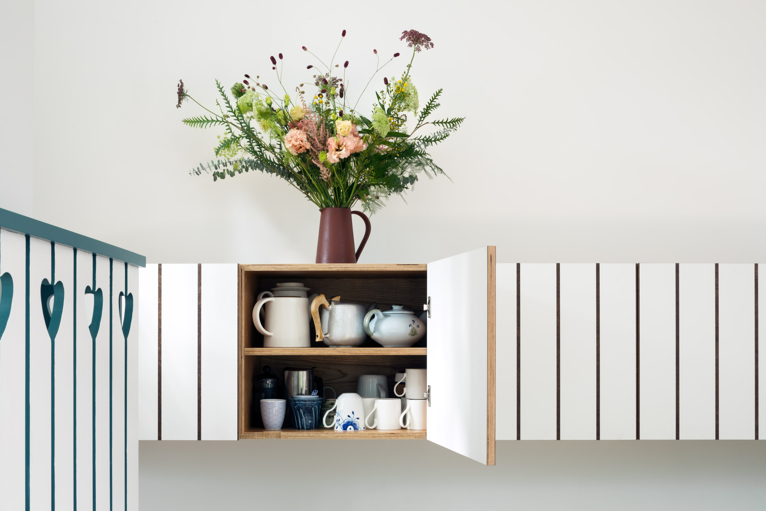 White wall cabinet with striped rebate detail. One open cupboard.