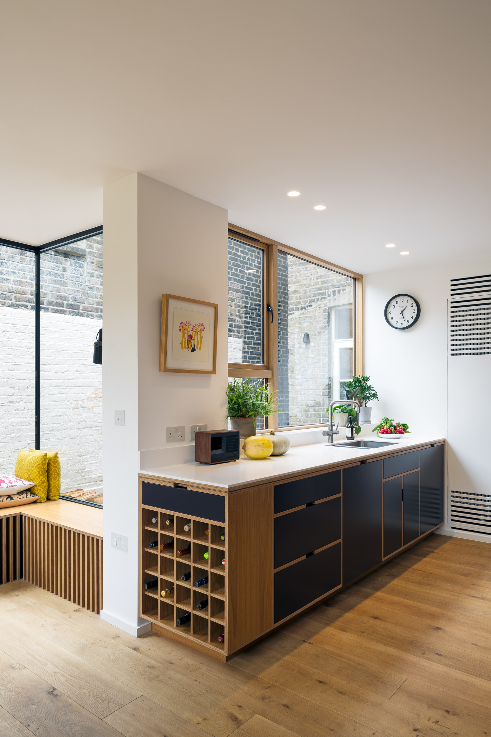 Black and plywood kitchen base units with winerack at the end and bench seating to cover radiator