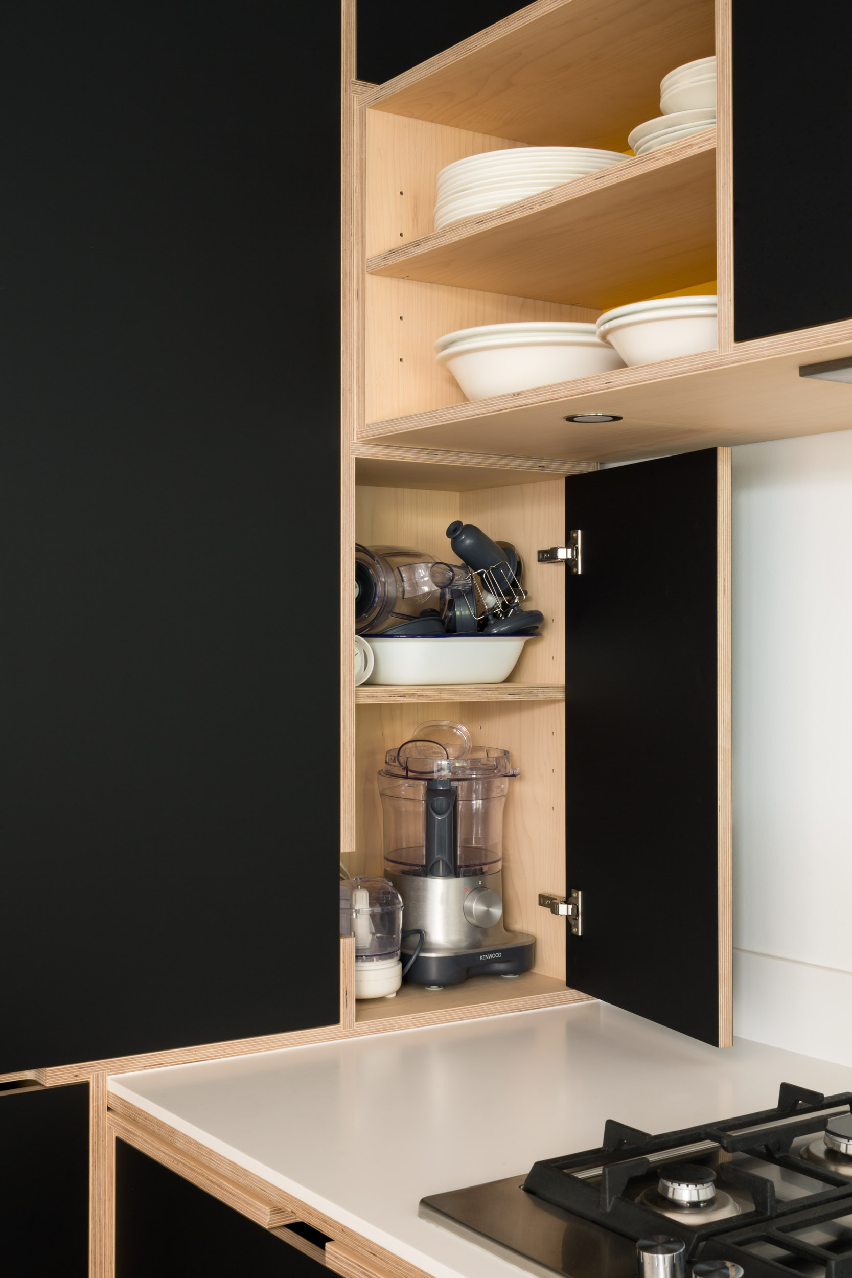 Plywood corner cupboard on worktop with black doors. Gas hob
