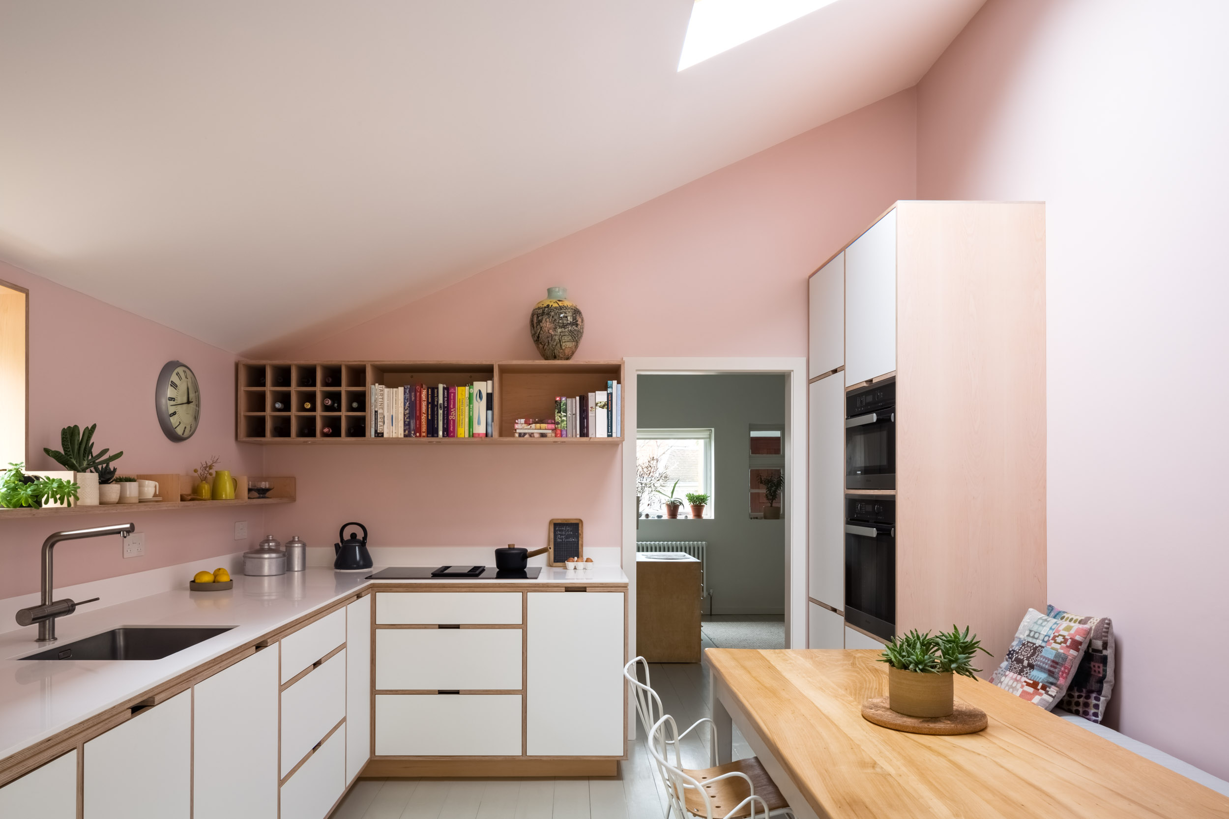 Pink walls and a maple plywood kitchen with open shelving
