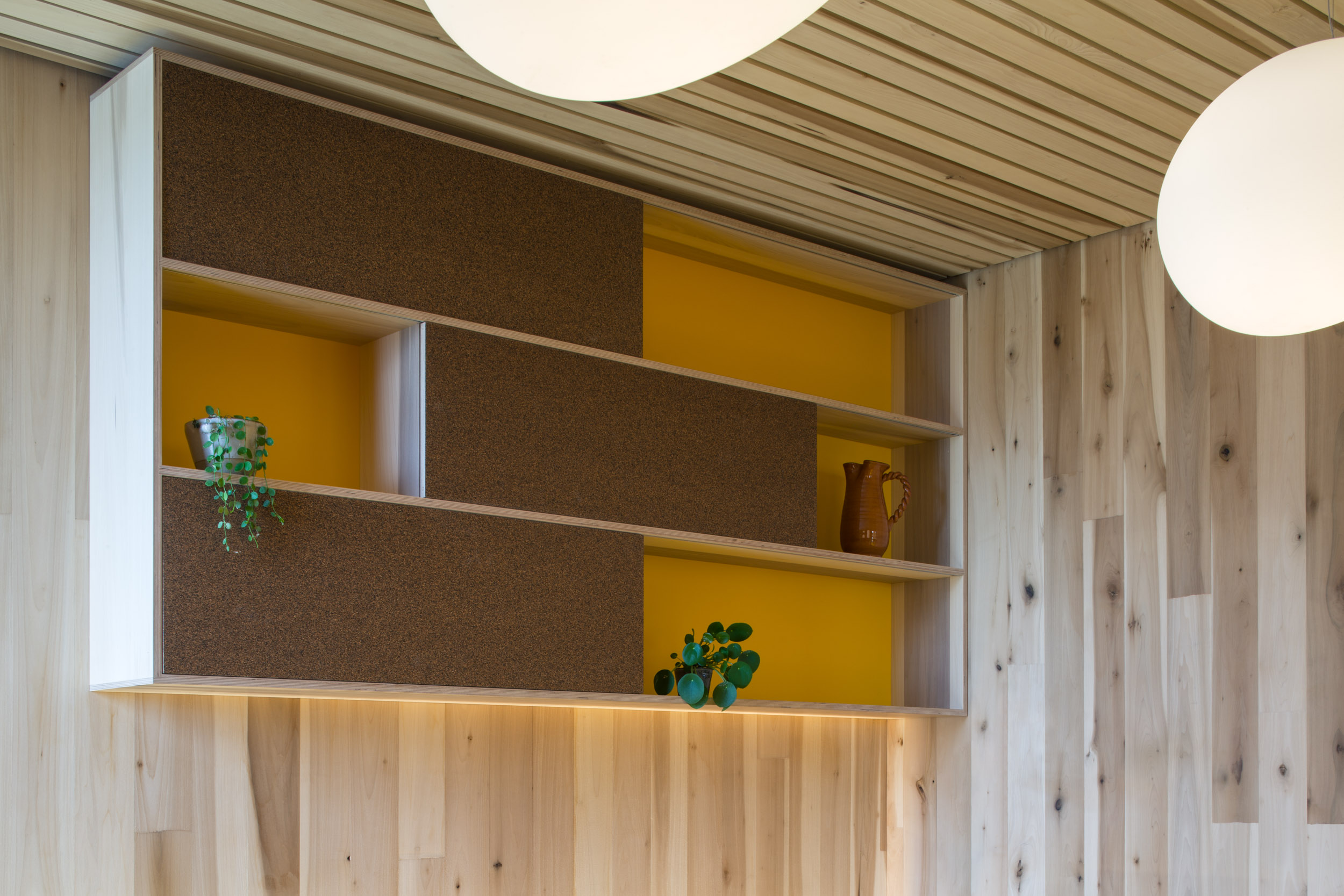 Shelving with a cork finish and yellow backdrop. CLT Maggies