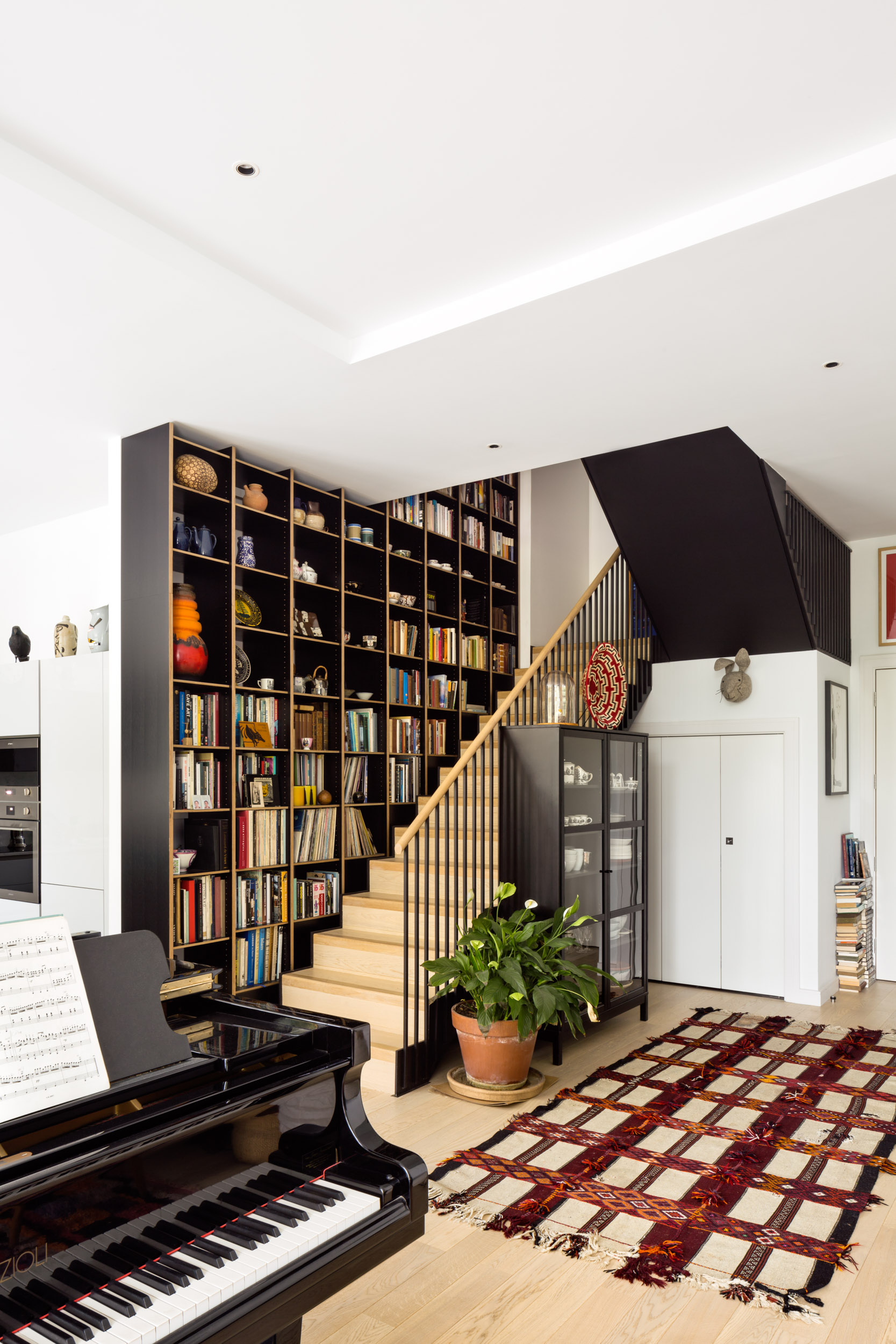 Dyed black veneer ply shelving over staircase with piano