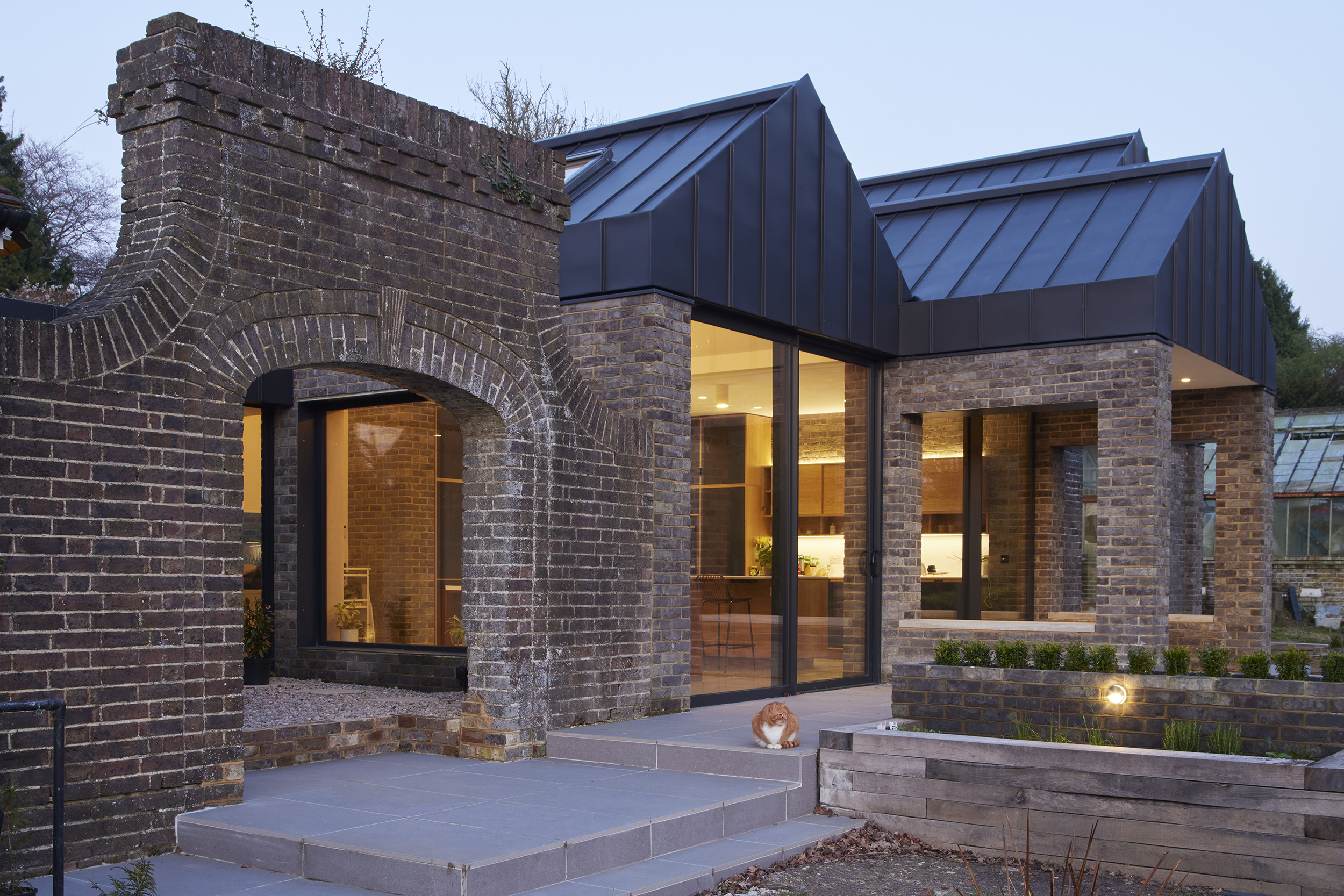 Contemporary brick extension with bespoke plywood kitchen by Uncommon Projects, featuring dark zinc roof forms, full-height glazing and restored period brickwork. Architecture by Selencky Parsons.