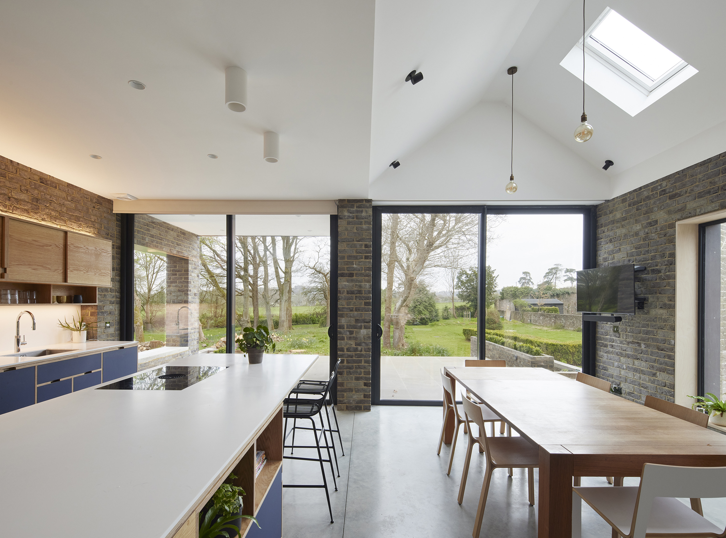 Open-plan dining and kitchen extension by Uncommon Projects with vaulted ceilings, exposed brickwork, large sliding glass doors and bespoke plywood joinery. Architecture by Selencky Parsons.