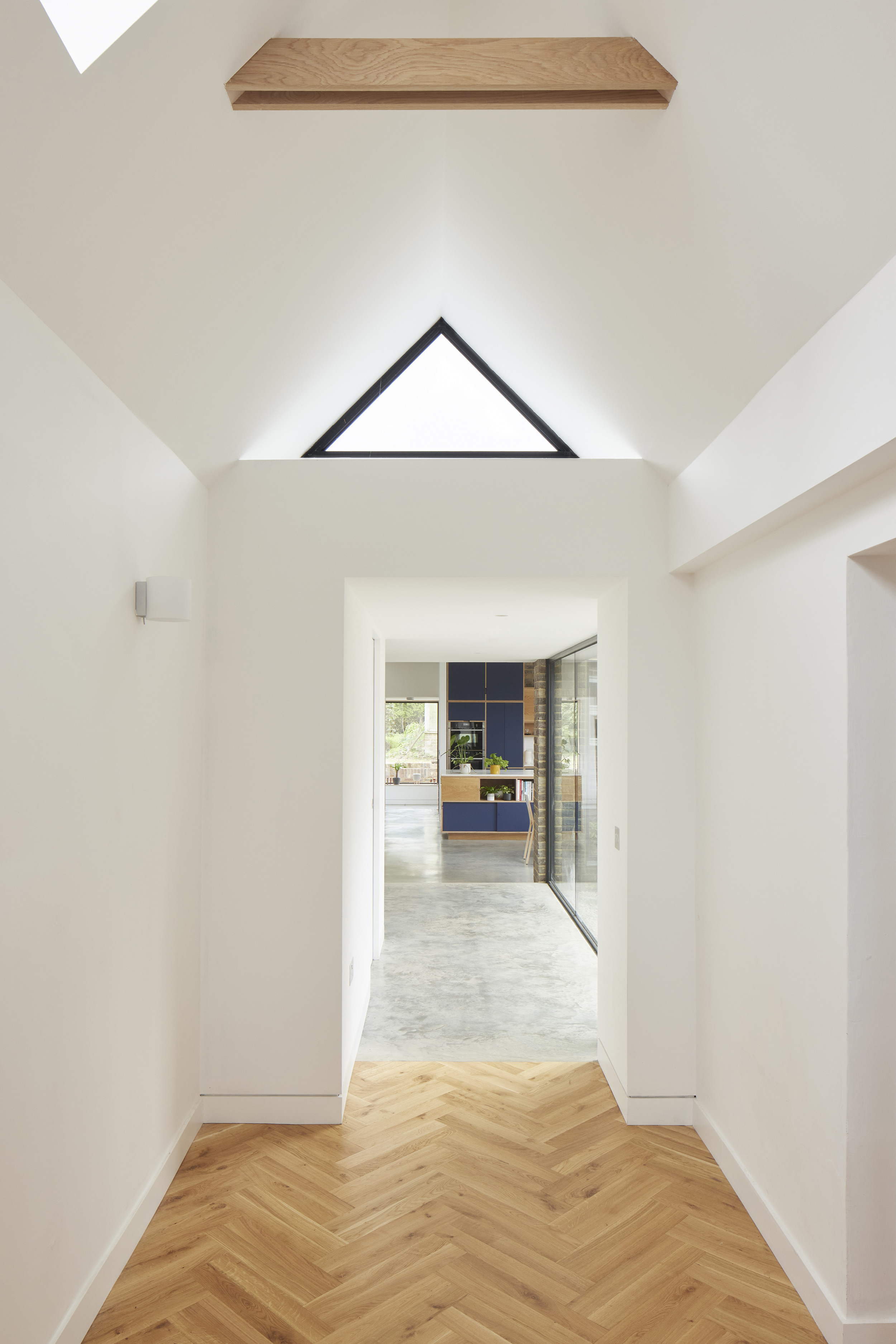 Minimal hallway leading into a modern plywood kitchen by Uncommon Projects, featuring polished concrete floor. Architecture by Selencky Parsons.