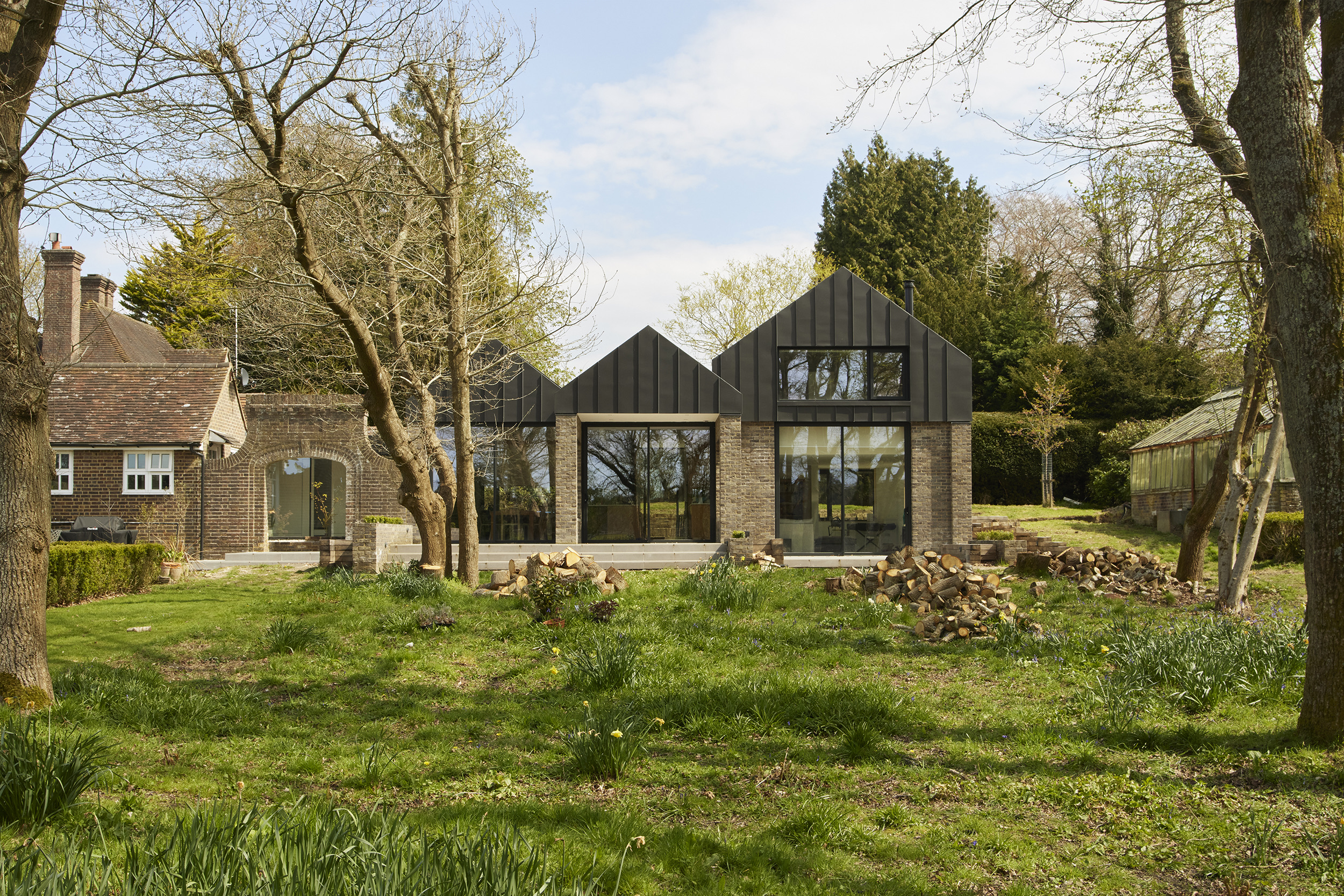 Modern bespoke kitchen by Uncommon Projects with blue plywood cabinetry, oak veneer shelving, white Corian worktops and expansive garden views. Architecture by Selencky Parsons.