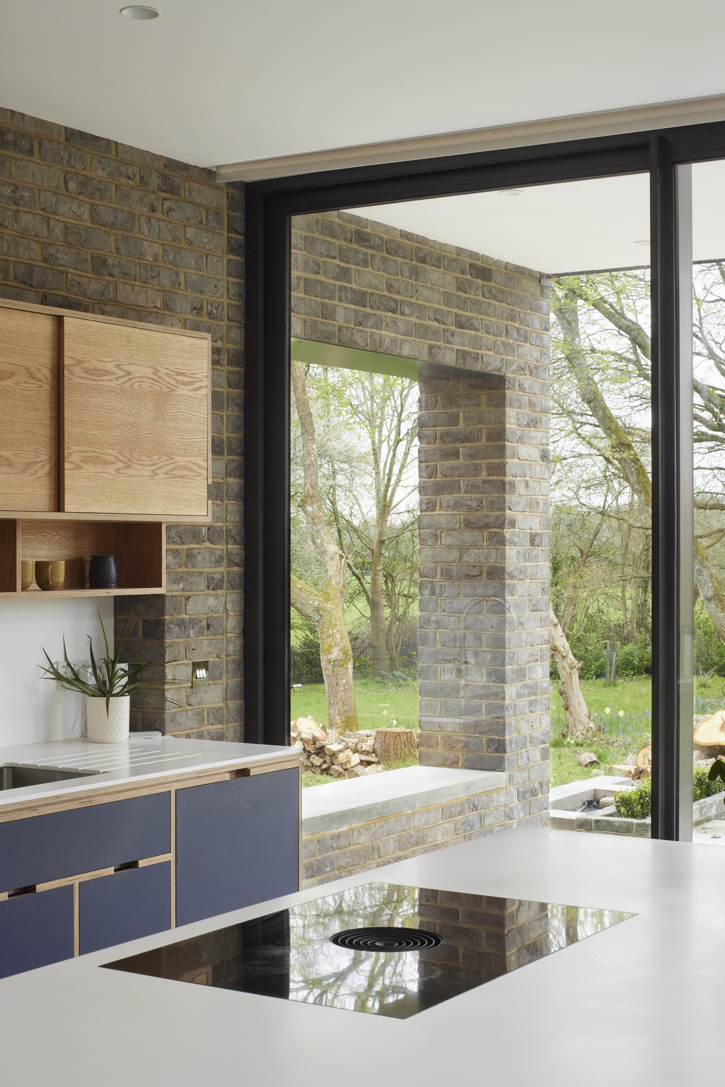 Bespoke plywood kitchen by Uncommon Projects with blue birch plywood cabinetry, white worktops and floor-to-ceiling glazing overlooking a rural garden Architecture by Selencky Parsons.