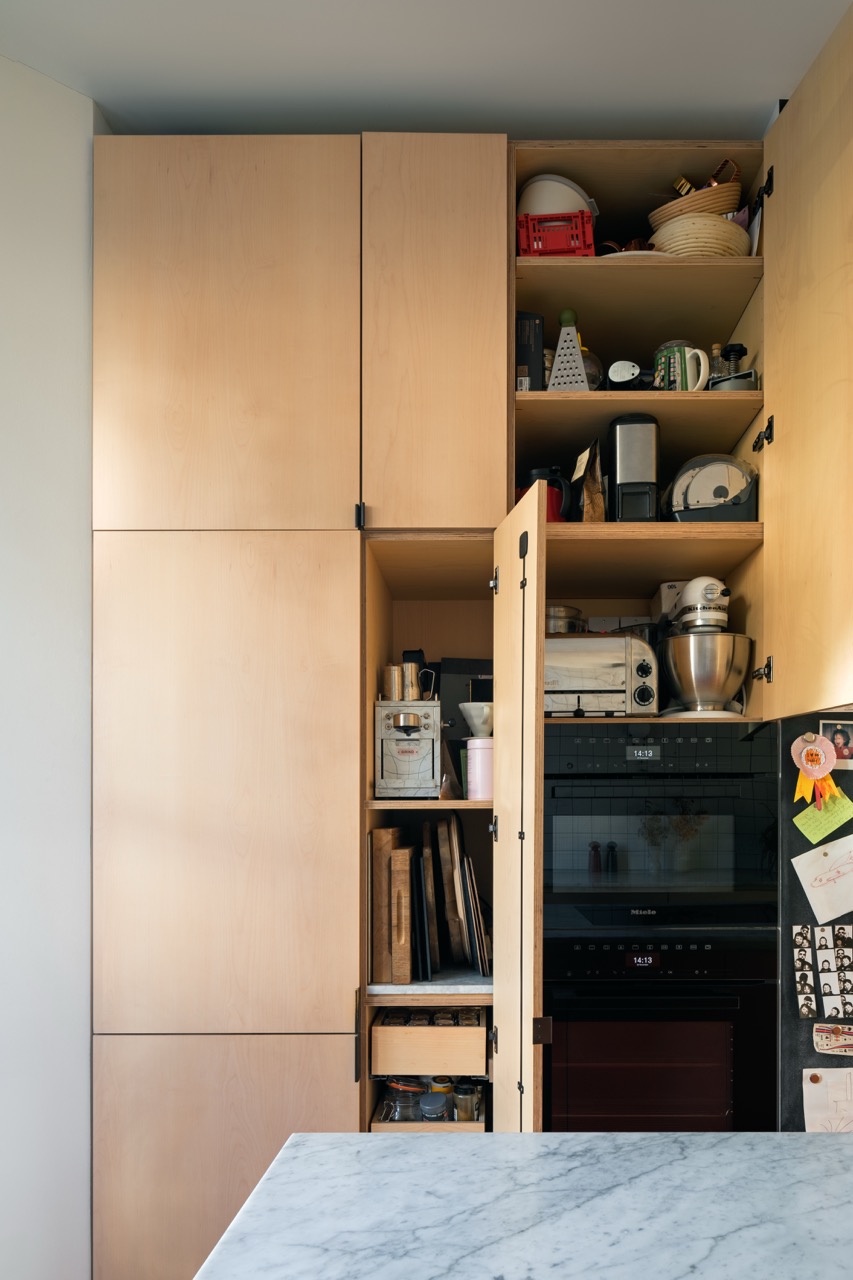 Open maple veneer pantry cabinet revealing kitchen storage and integrated Miele double ovens