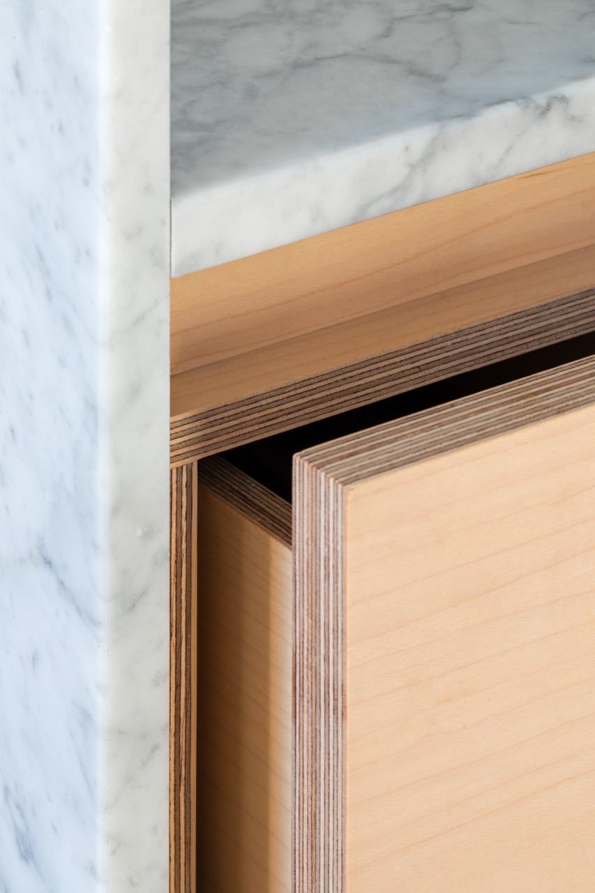 Close detail of maple veneer drawer front and exposed plywood edge beneath Carrara marble worktop