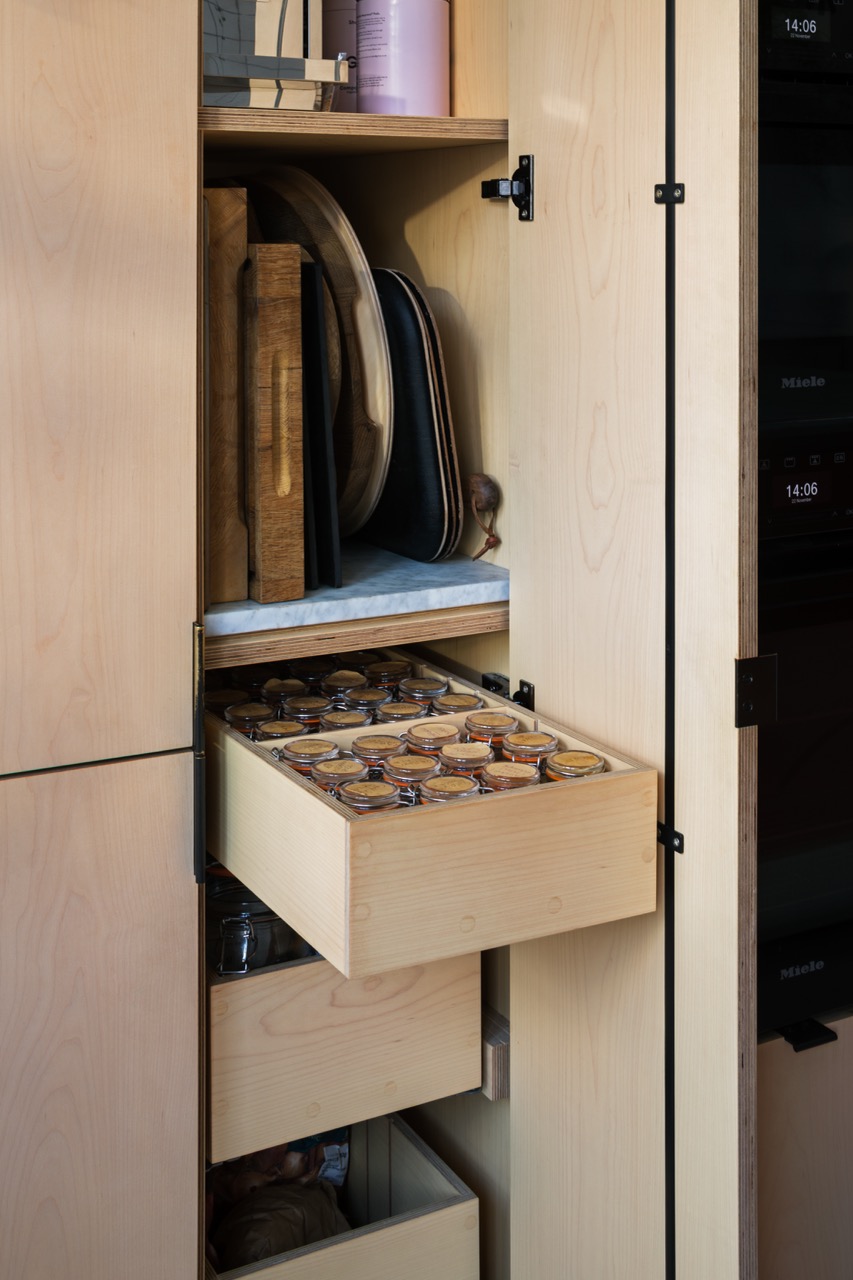 Open pantry cabinet with pull-out plywood drawer storing cutting boards, spice jars, bespoke kitchen by Uncommon Projects
