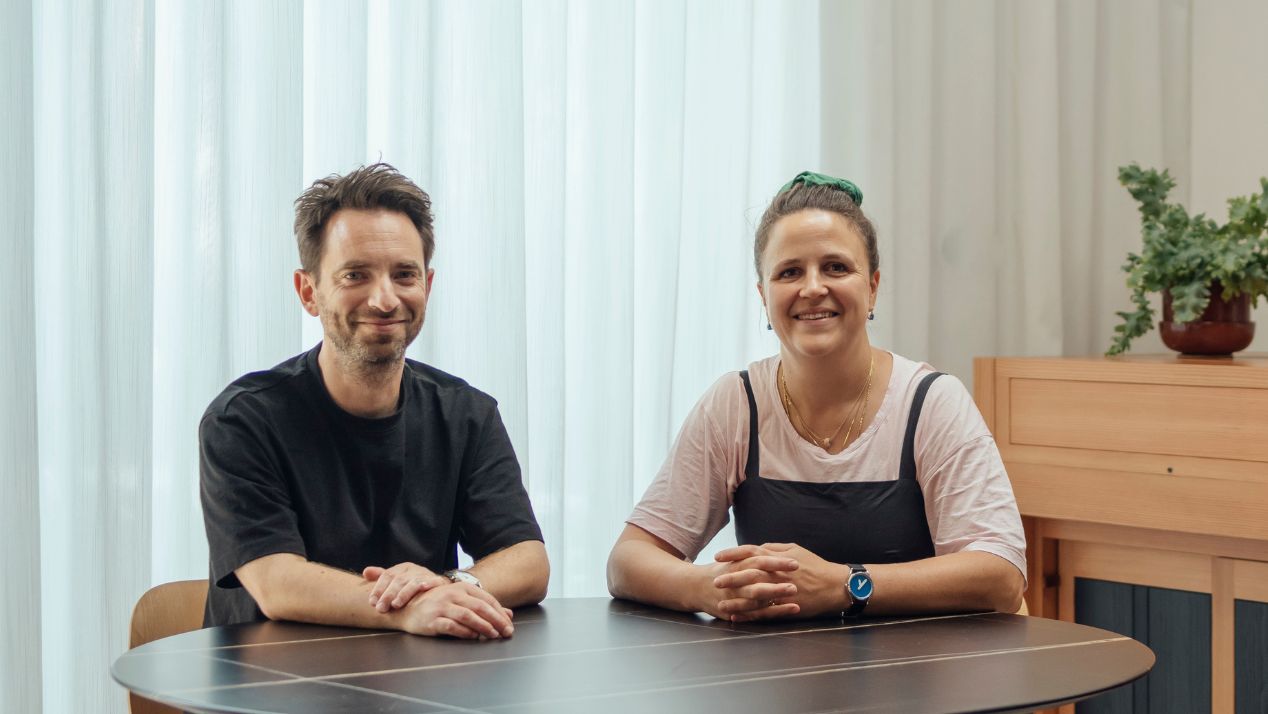    Archmongers founders Johan Hybschmann and Margaret Bursa seated together at a table in a contemporary interior.