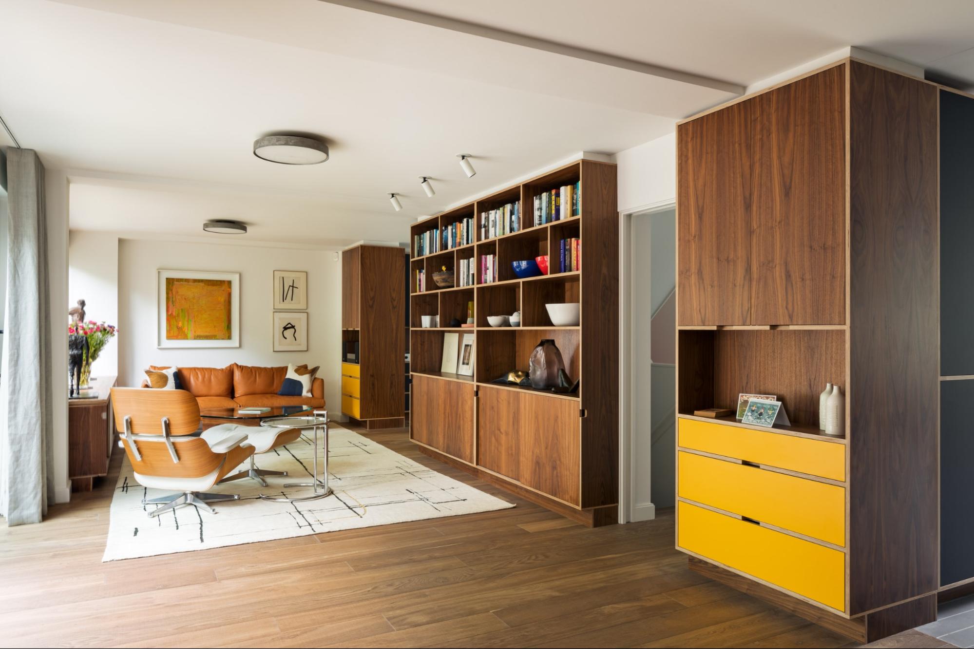Walnut-veneered plywood storage wall with bookshelves and yellow drawers in a mid-century style living room