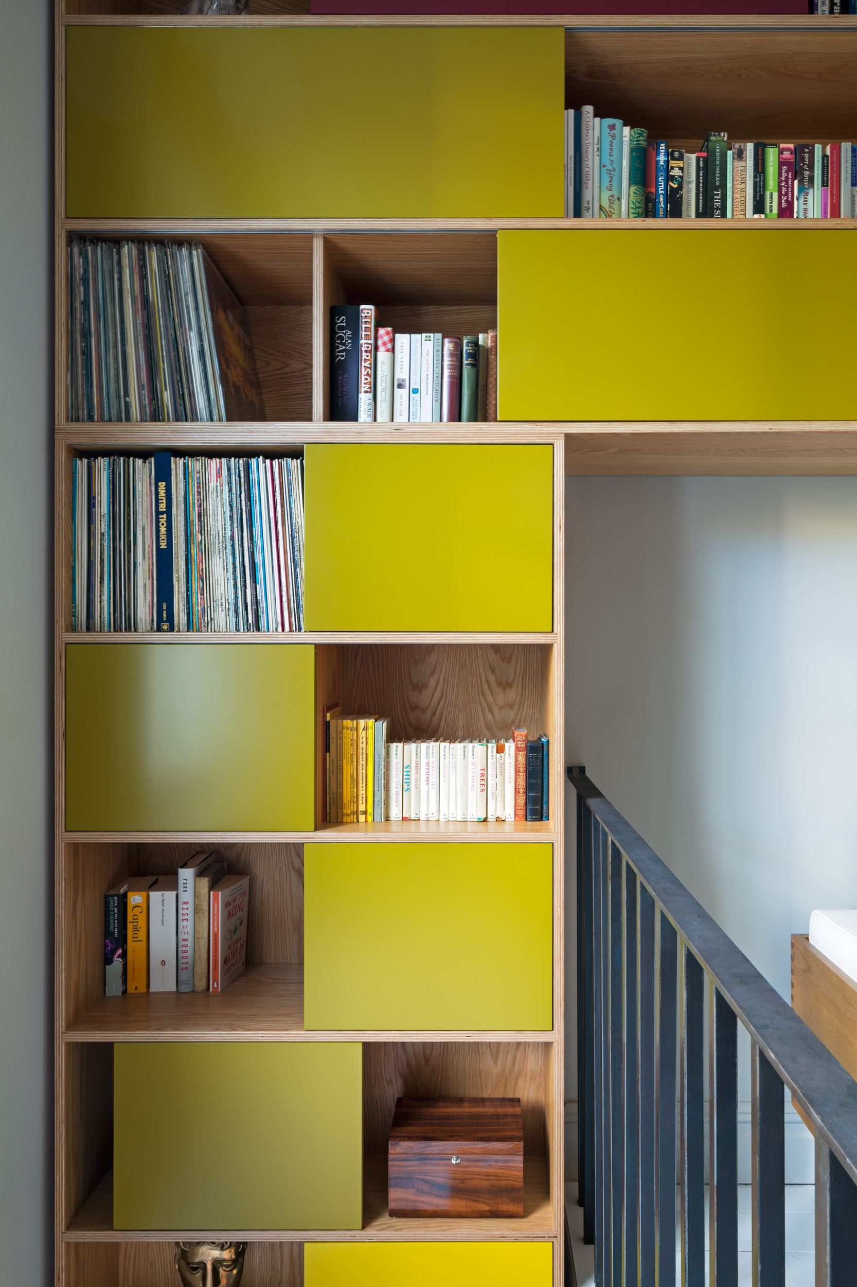 Stepped plywood shelving with chartreuse sliding doors climbing a staircase, sized for vinyl and books