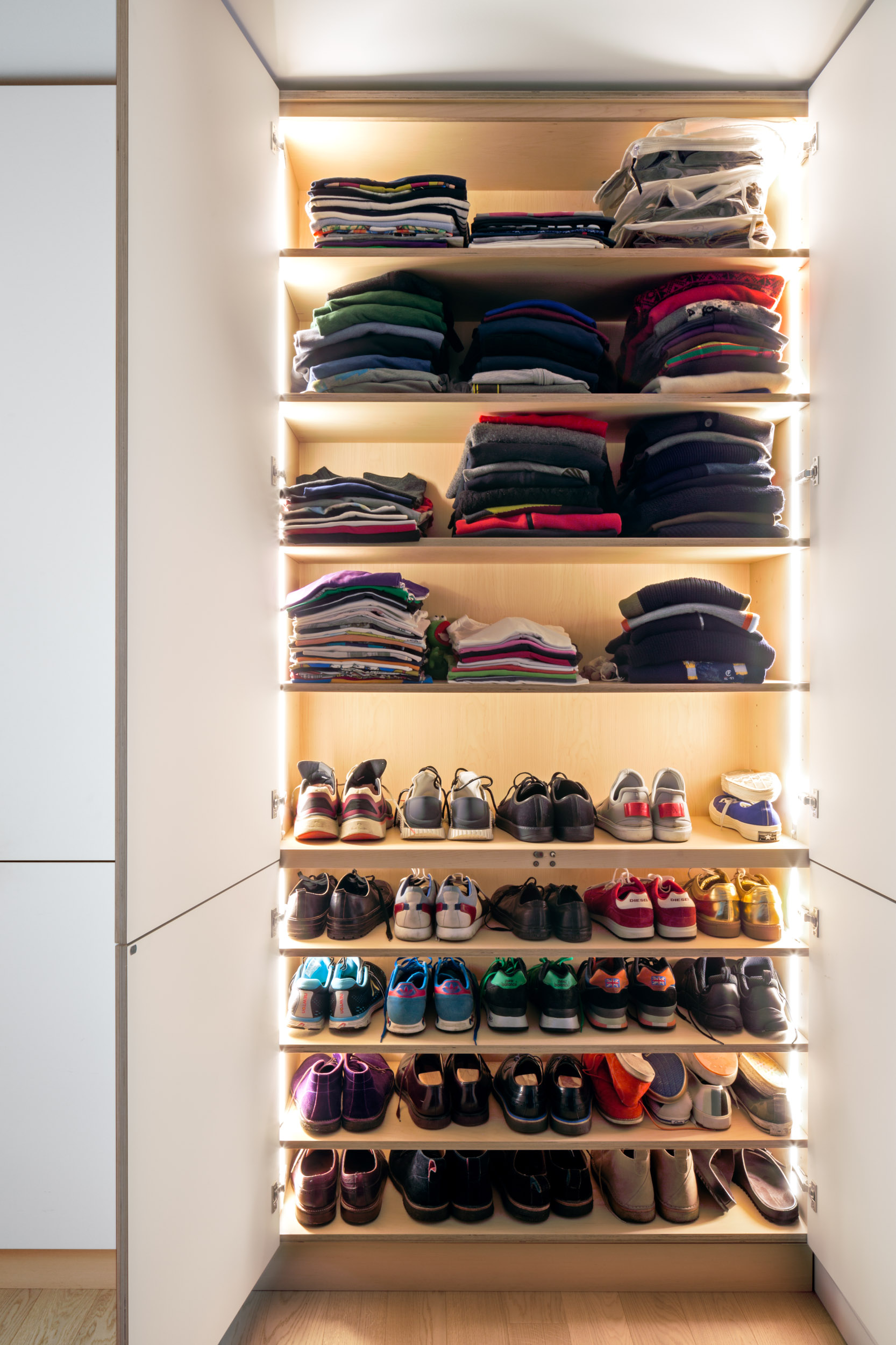 Tall bespoke plywood wardrobe with internally lit shelves for folded knitwear and shoes.