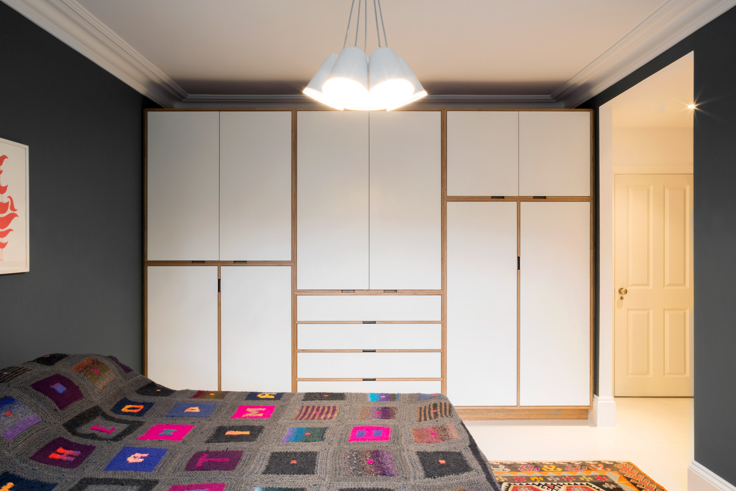 White bespoke fitted wardrobes with oak-trimmed plywood edges wrapping a bedroom doorway.
