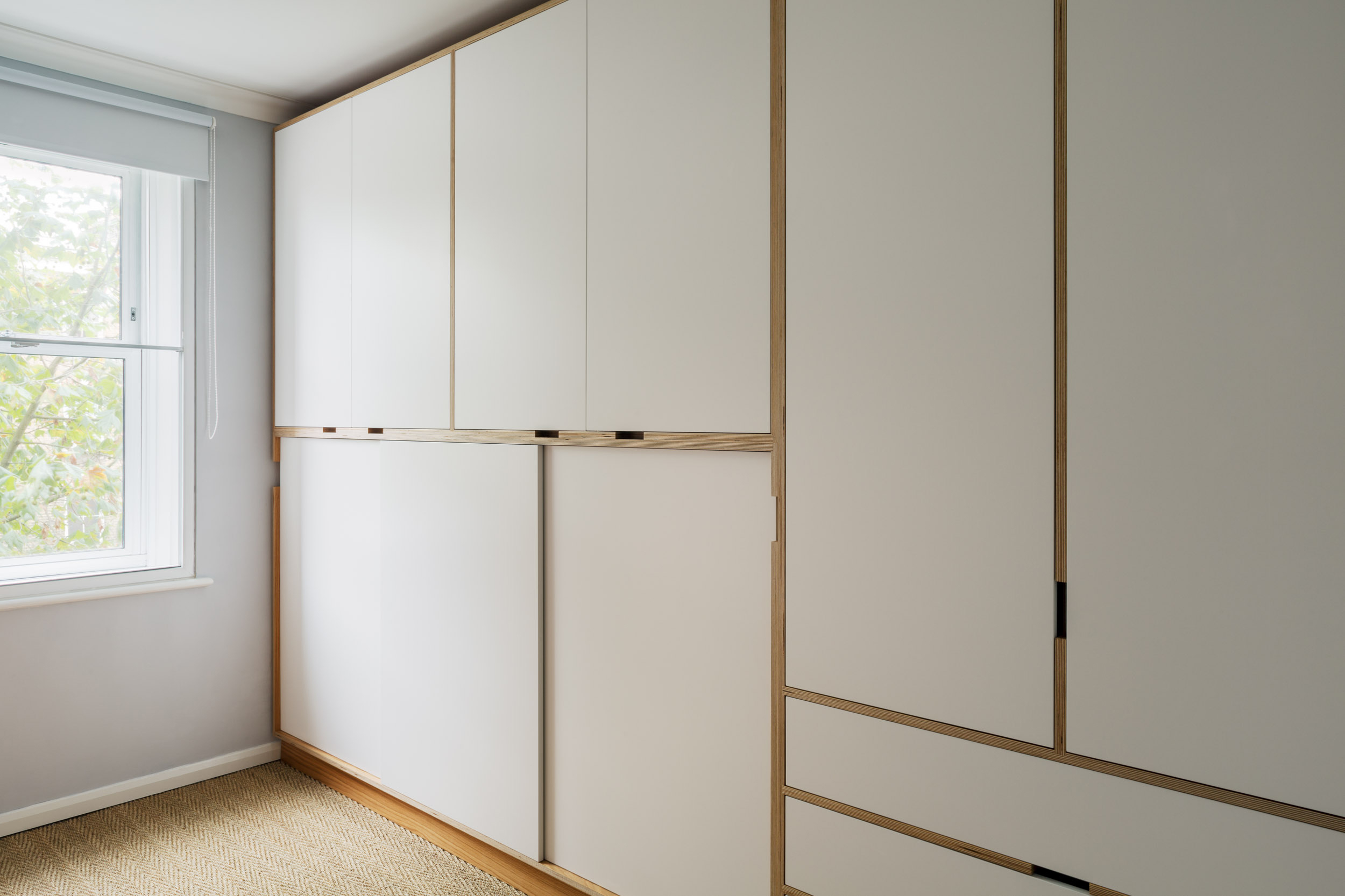 Cream bespoke fitted wardrobes with oak edges, built into a sloping loft ceiling.