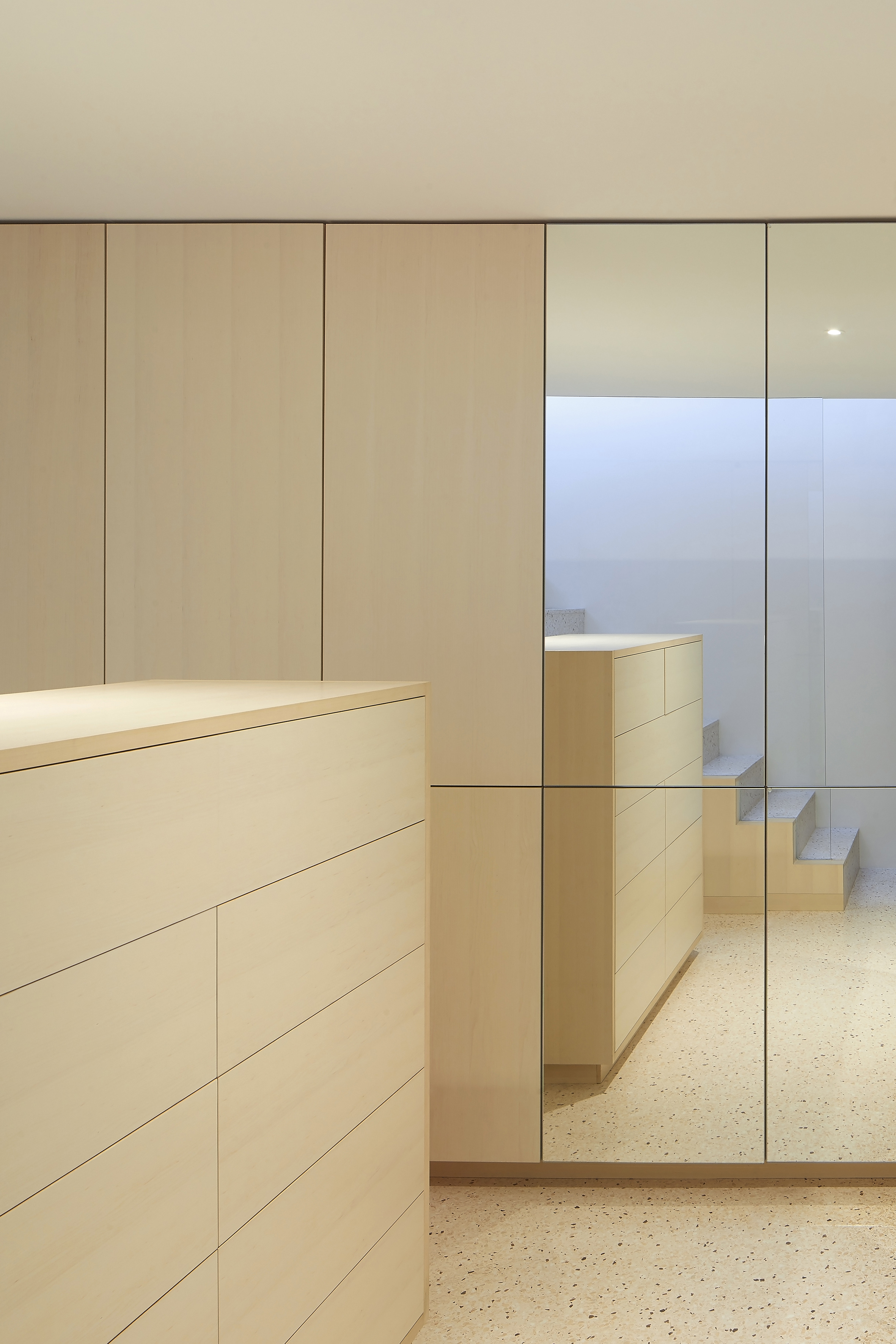 Minimalist maple plywood dressing room with a full-height mirrored wardrobe and built-in drawers.