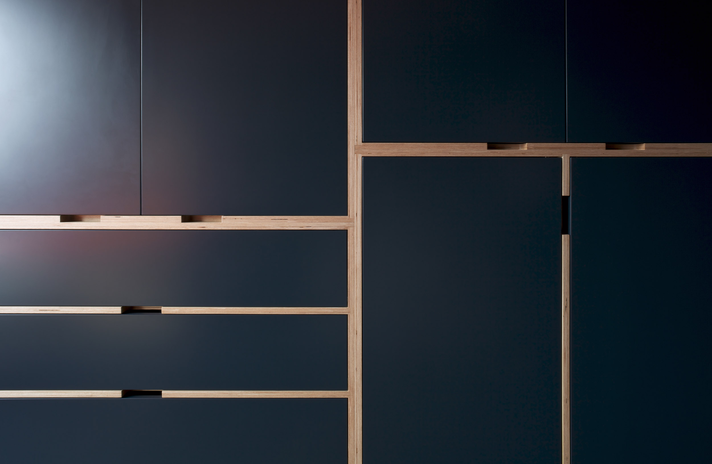 Detail of navy fitted wardrobe doors and drawers framed by exposed birch plywood edges.