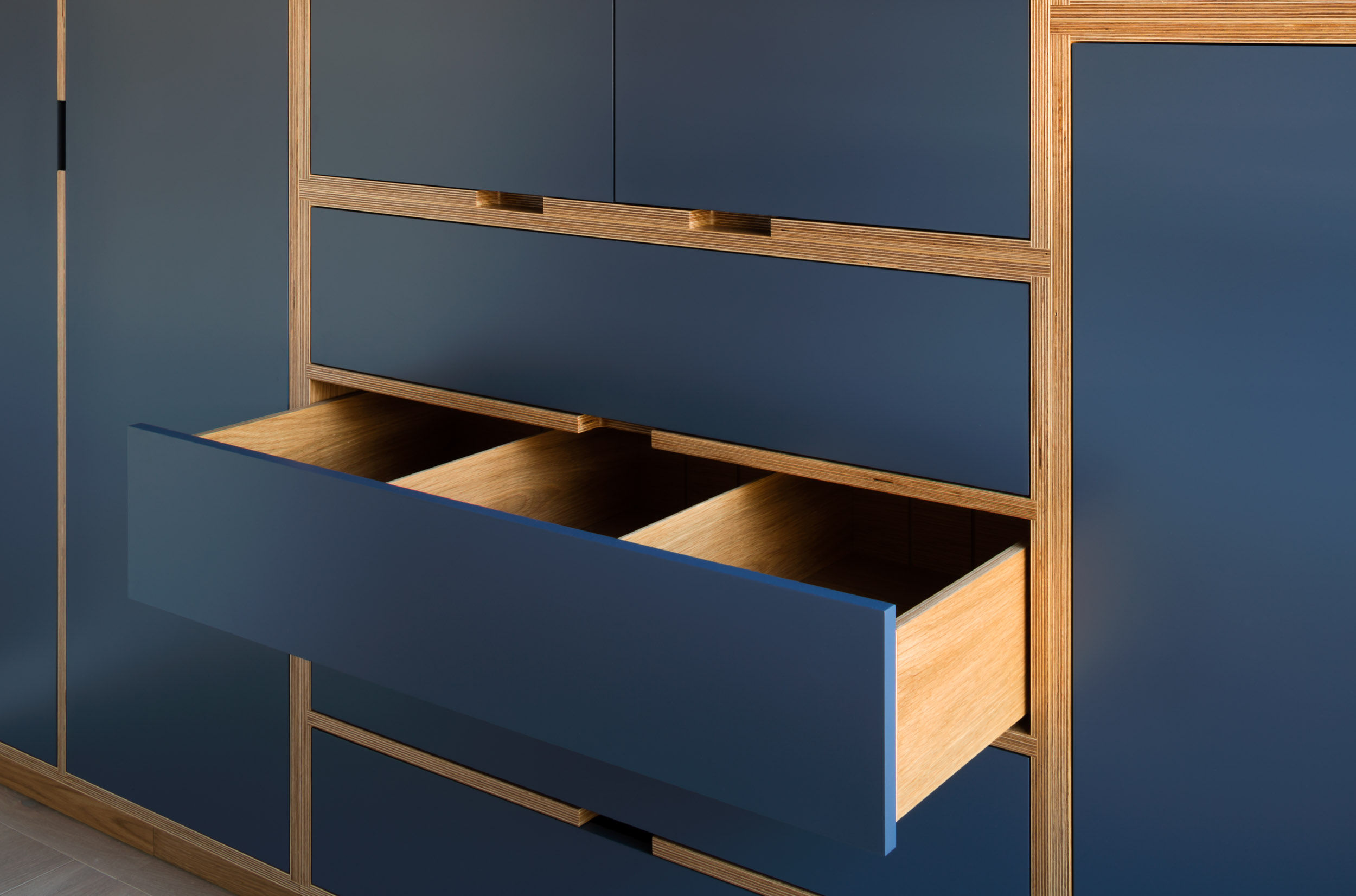 Navy blue plywood wardrobe drawer pulled open, with a compartmentalised oak interior and birch ply edges.