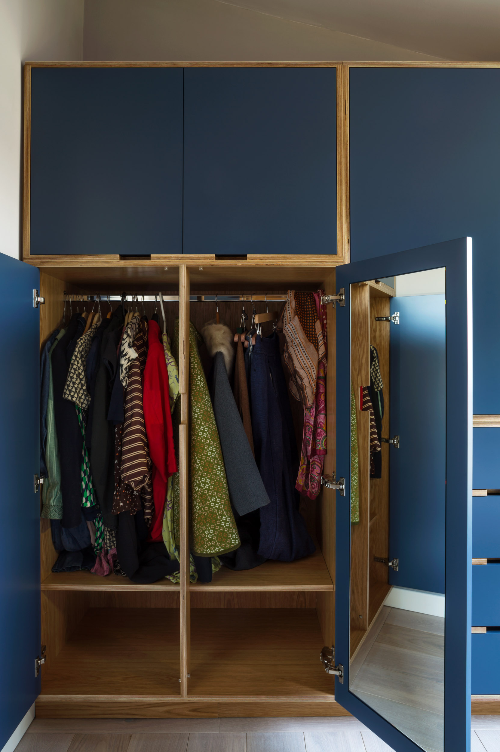 Bespoke blue fitted wardrobe with doors open, showing oak-lined hanging space and an inset mirror.