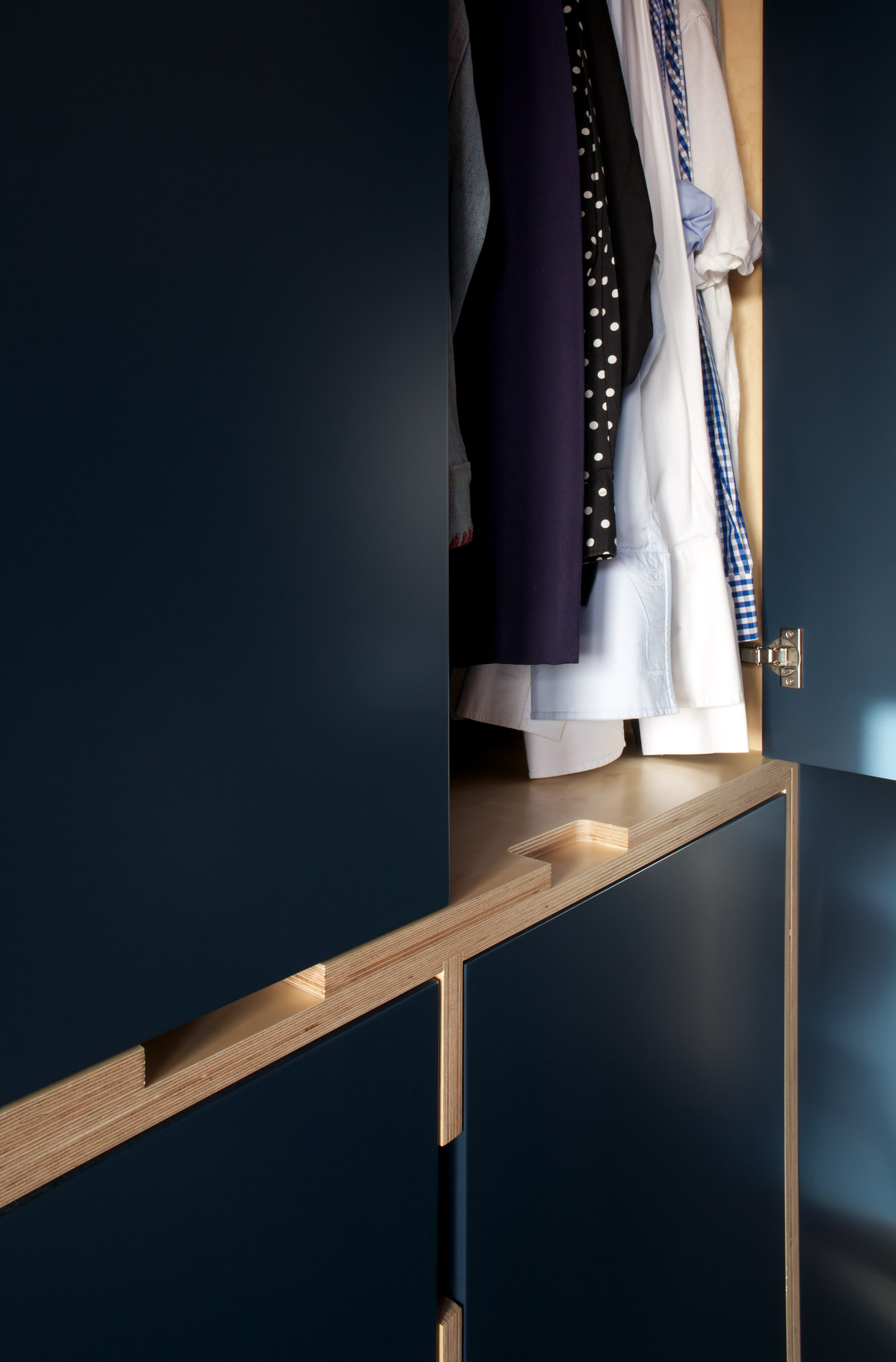 Navy plywood wardrobe with a handle cut into the ply edge and integrated interior lighting.
