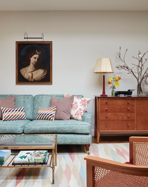 Layered sitting room with a patterned blue sofa, mixed cushions, an antique portrait, a mid-century sideboard and a harlequin rug