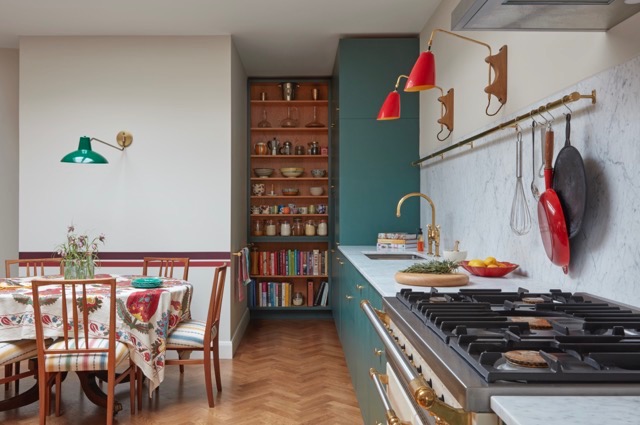 Deep green shaker-style plywood kitchen with marble splashback, brass utensil rail and range cooker beside a parquet dining area