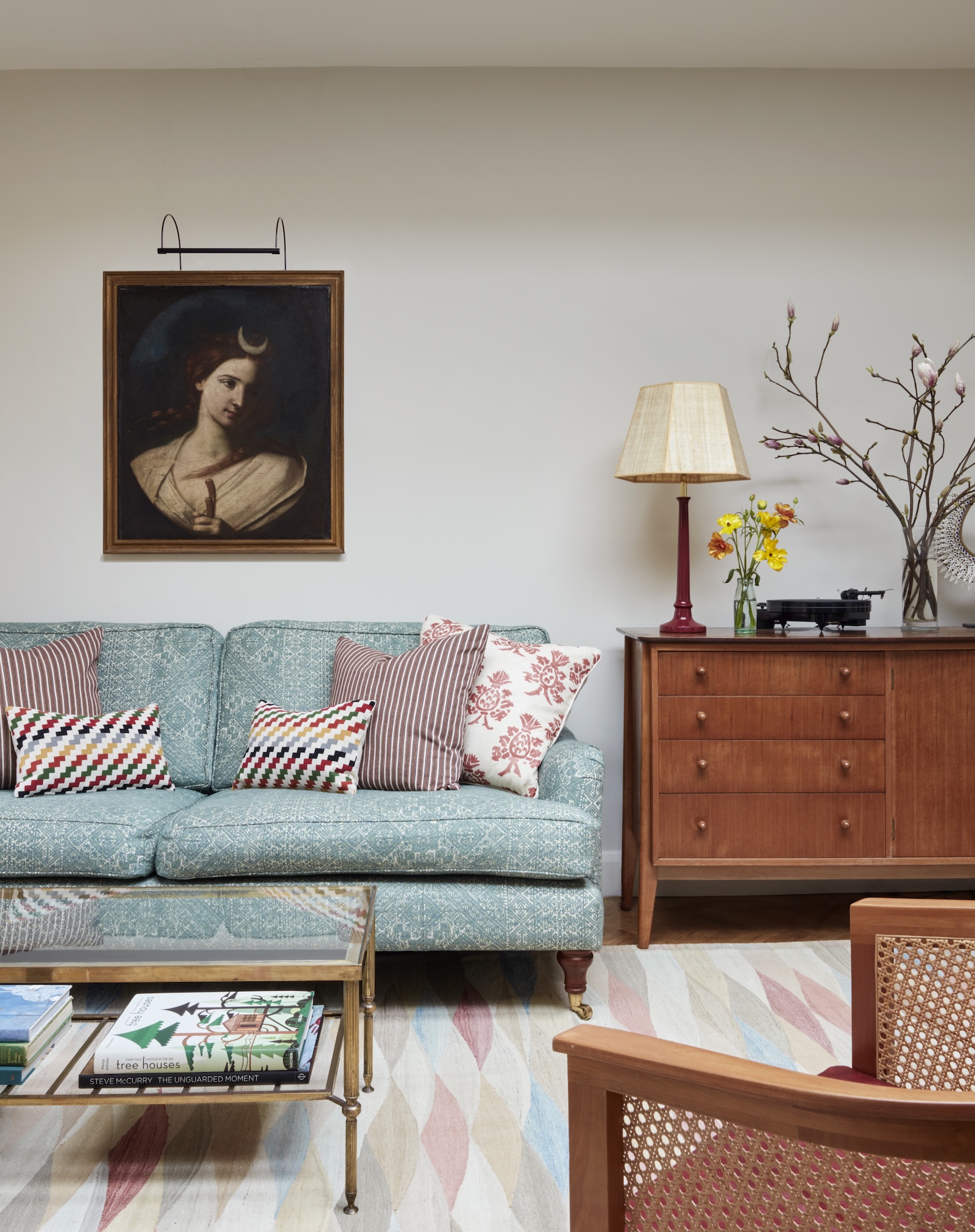 Layered sitting room with a patterned blue sofa, mixed cushions, an antique portrait, a mid-century sideboard and a harlequin rug
