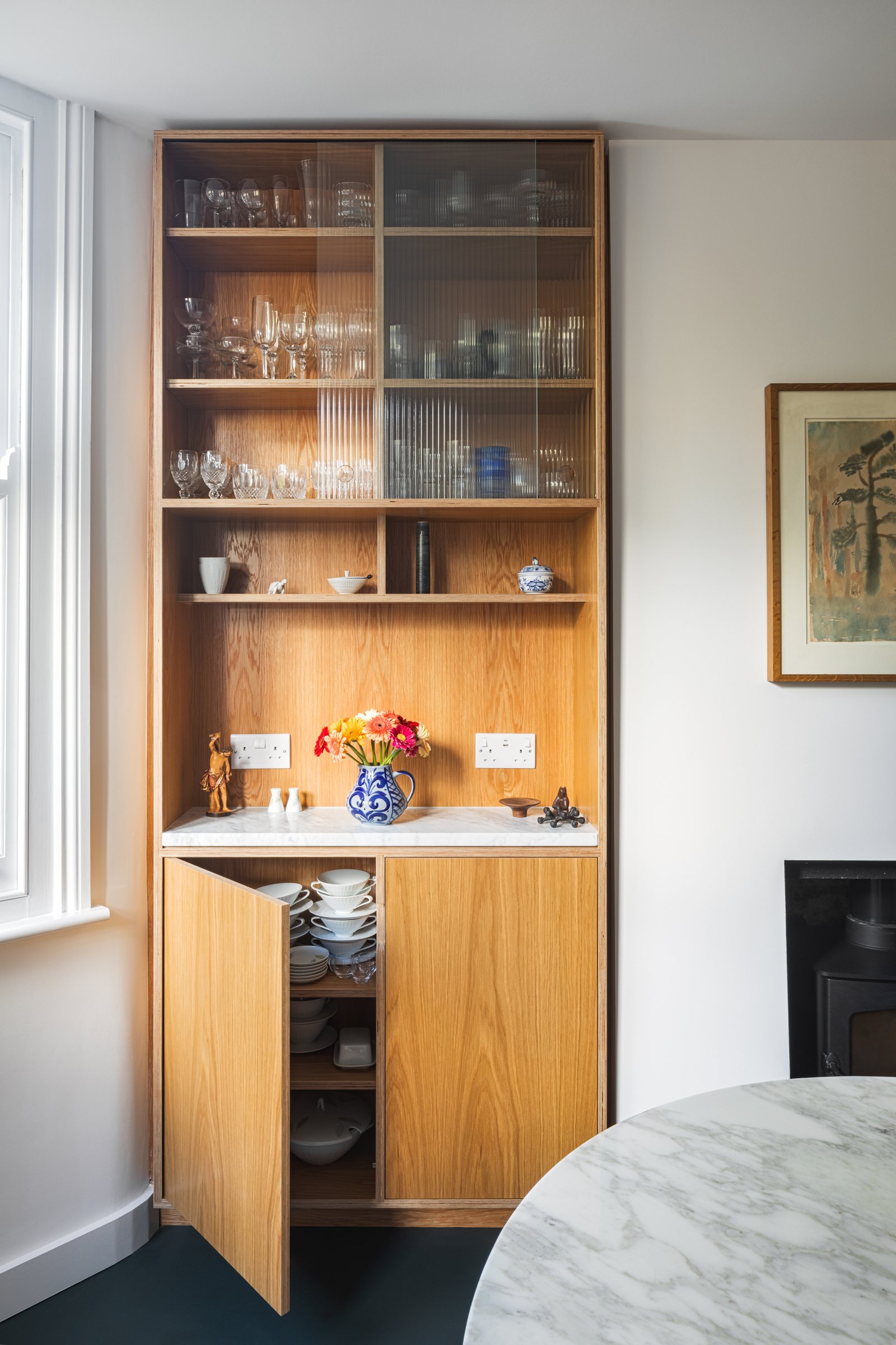 Open oak cupboard revealing stacked porcelain bowls below a fluted glass cabinet of glassware