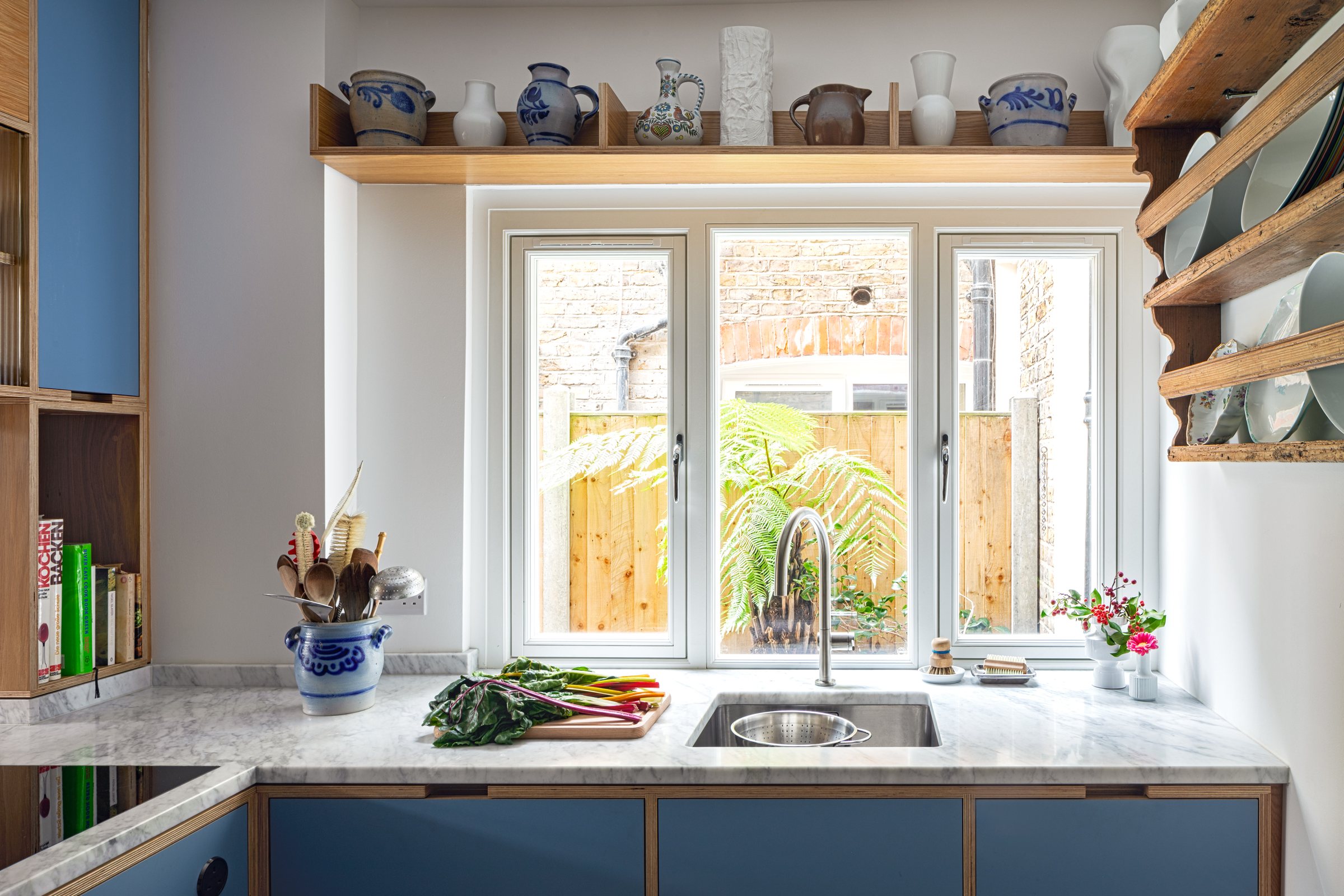 Undermounted stainless steel sink in a Carrara marble worktop beneath a garden window, bespoke plywood kitchen