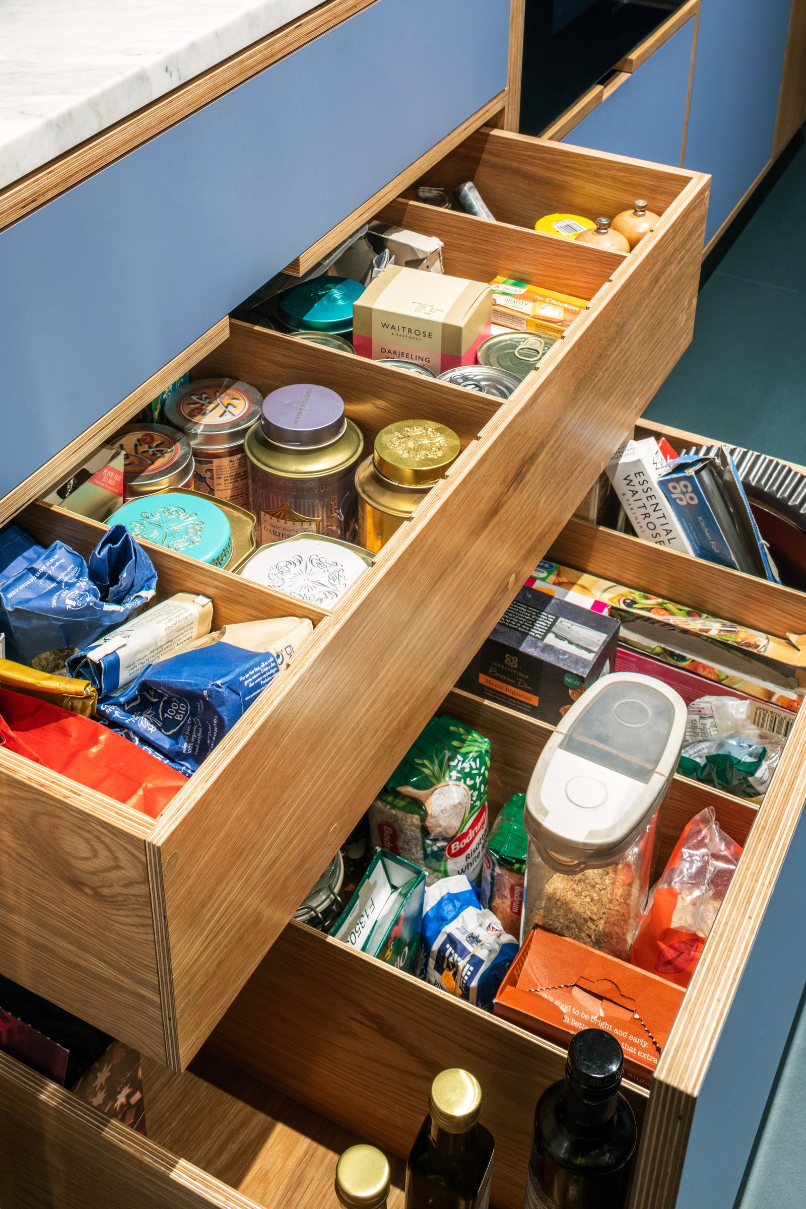 Internal pantry drawers in oak plywood holding tins, jars and dry goods behind a blue laminate front