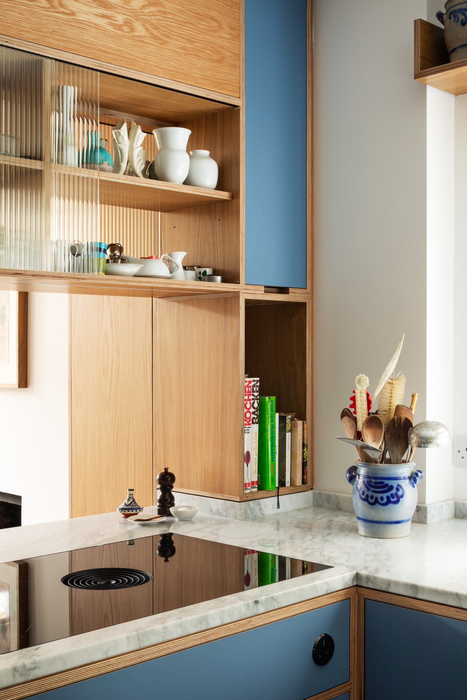 Corner of a bespoke plywood kitchen with Bora hob, fluted glass display cabinet and an oak niche for cookbooks