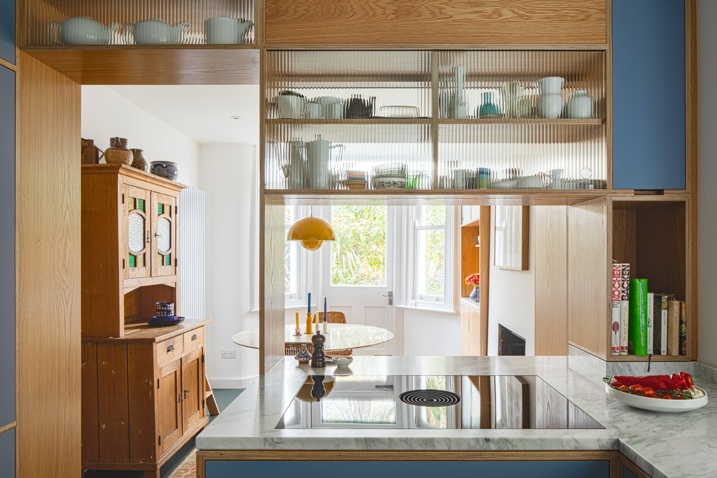 View over a Bora hob through the hatch to the dining room, with porcelain displayed on oak shelves above
