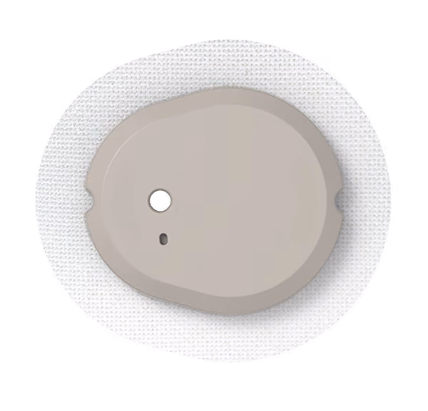 Close-up of a small, beige device with two holes, adhered to white textured fabric, resembling a medical sensor patch.